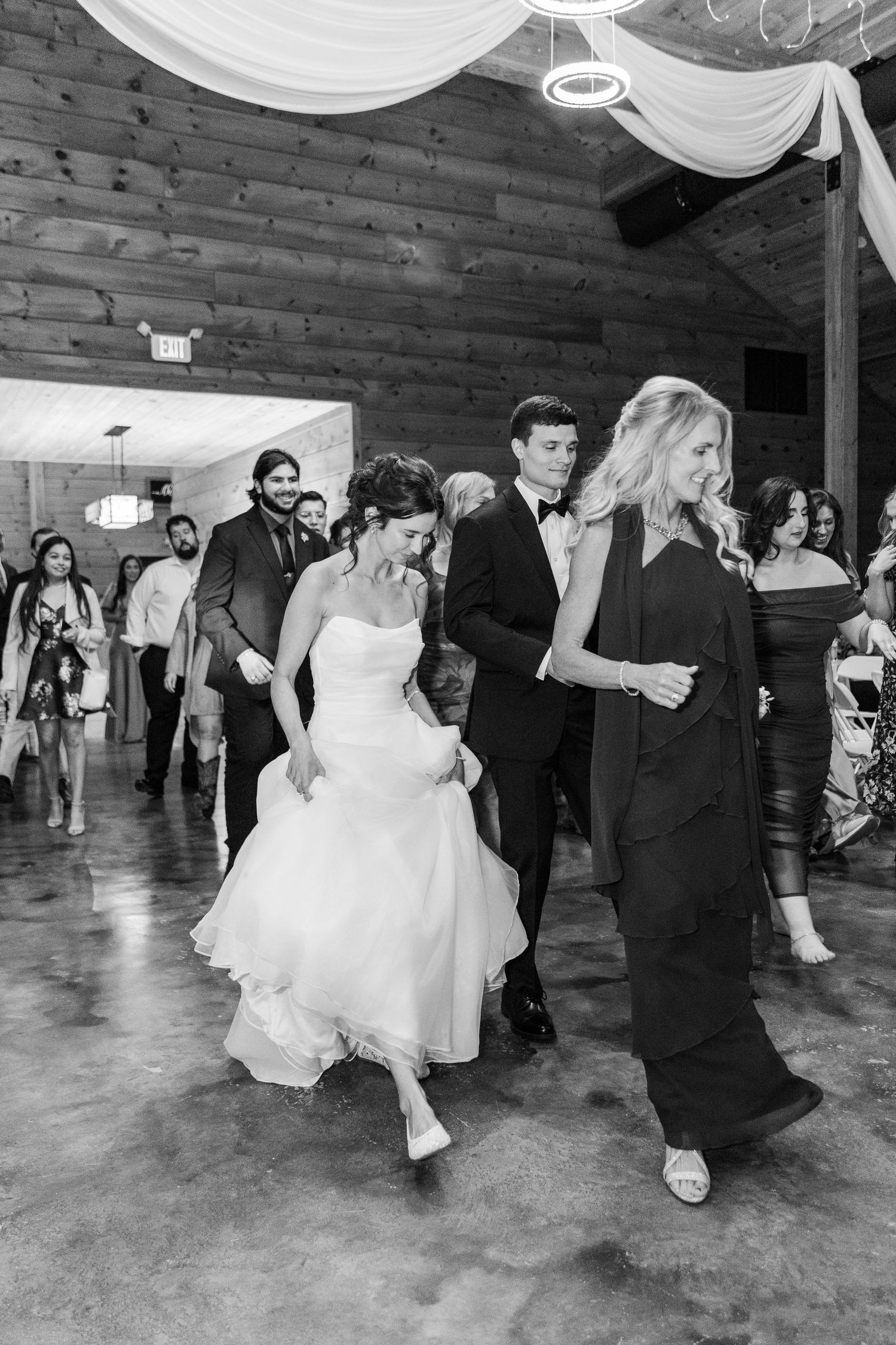 Wedding guests dance and celebrate on a rustic brick-walled dance floor decorated with elegant white fabric draping.