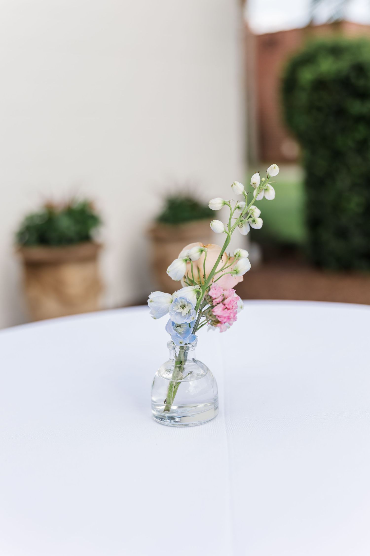 Small glass bud vases with dainty pink and white flowers create a minimalist table setting progression.