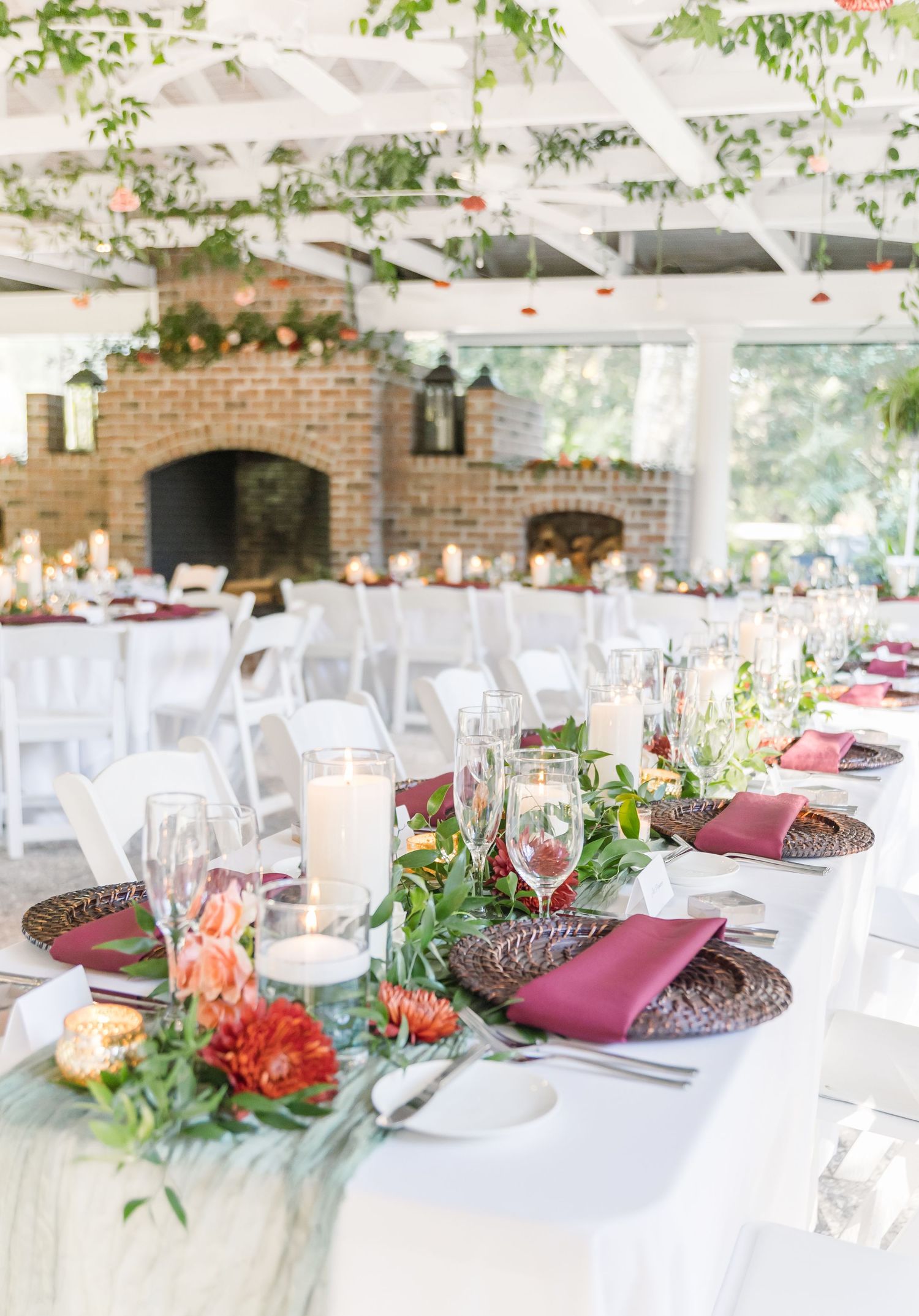 Elegant wedding reception setup with white tables, burgundy napkins, and coral floral centerpieces in a rustic brick venue.