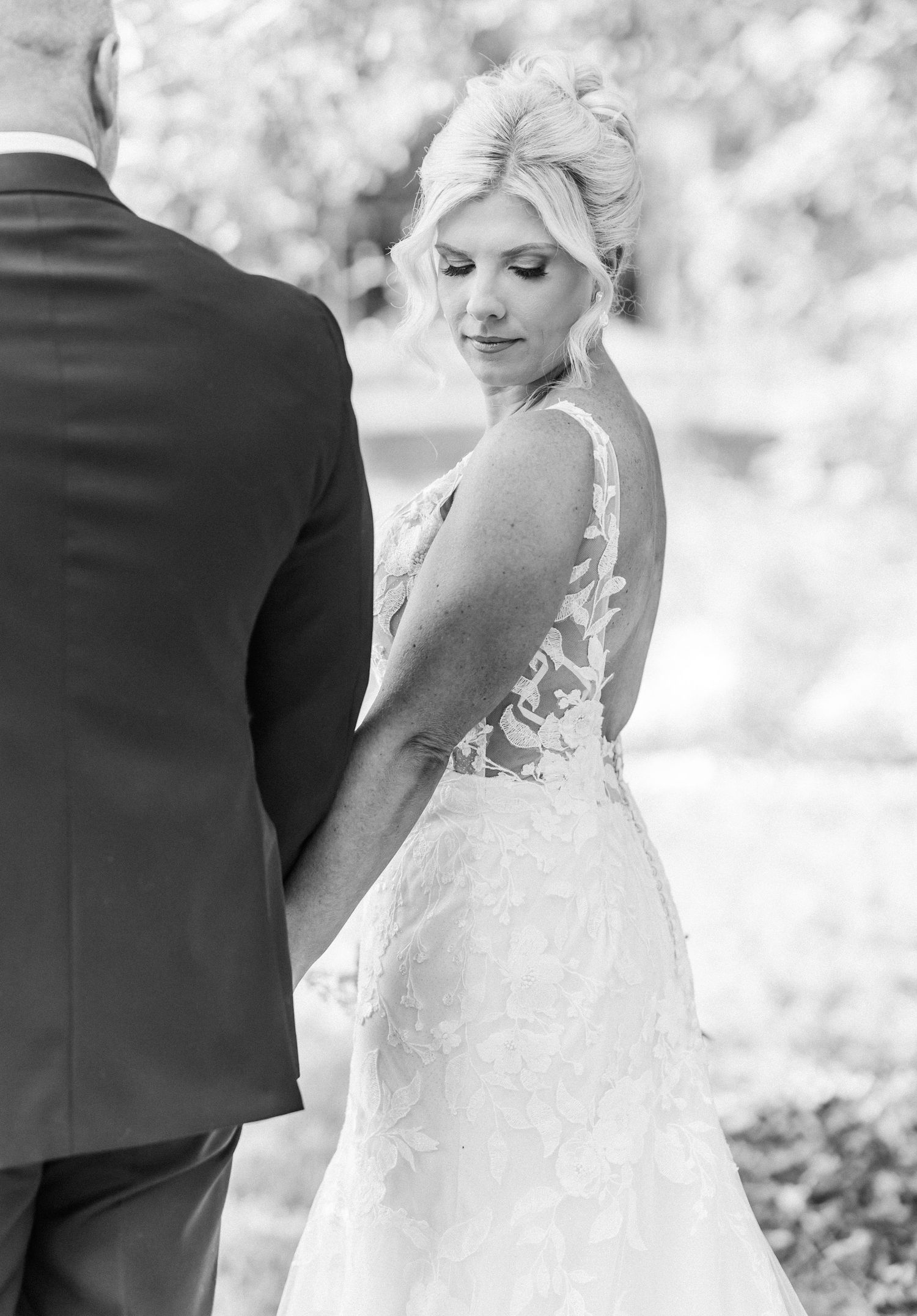 A romantic black and white wedding photo showing a couple in formal attire embracing outdoors.