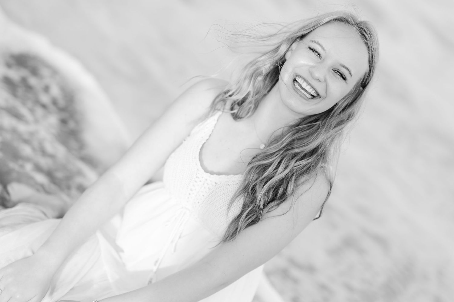 A black and white close-up beach portrait captures wind-swept hair and a natural smile.