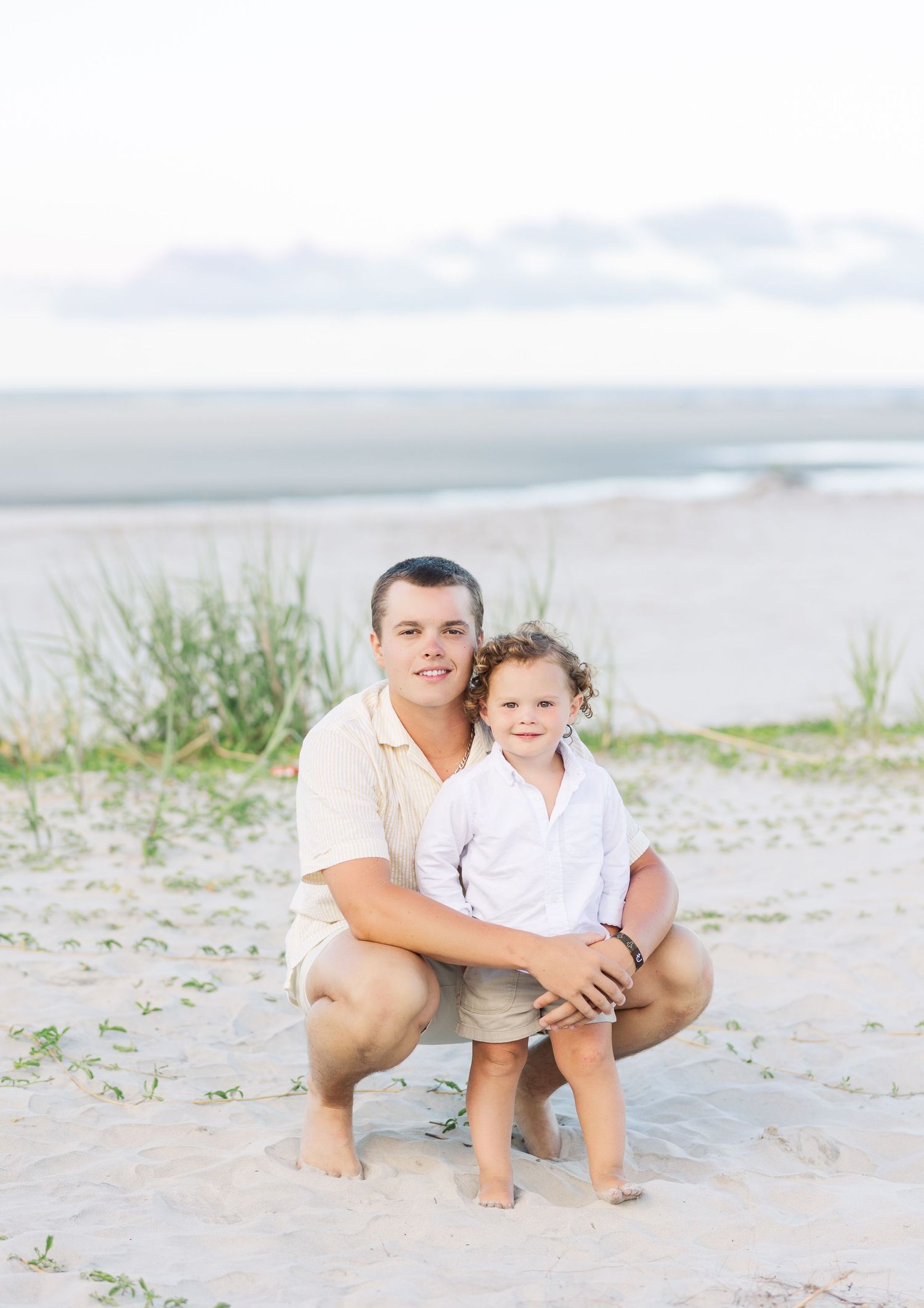A heartwarming moment captured on a sandy beach as an adult and child pose together by the water.