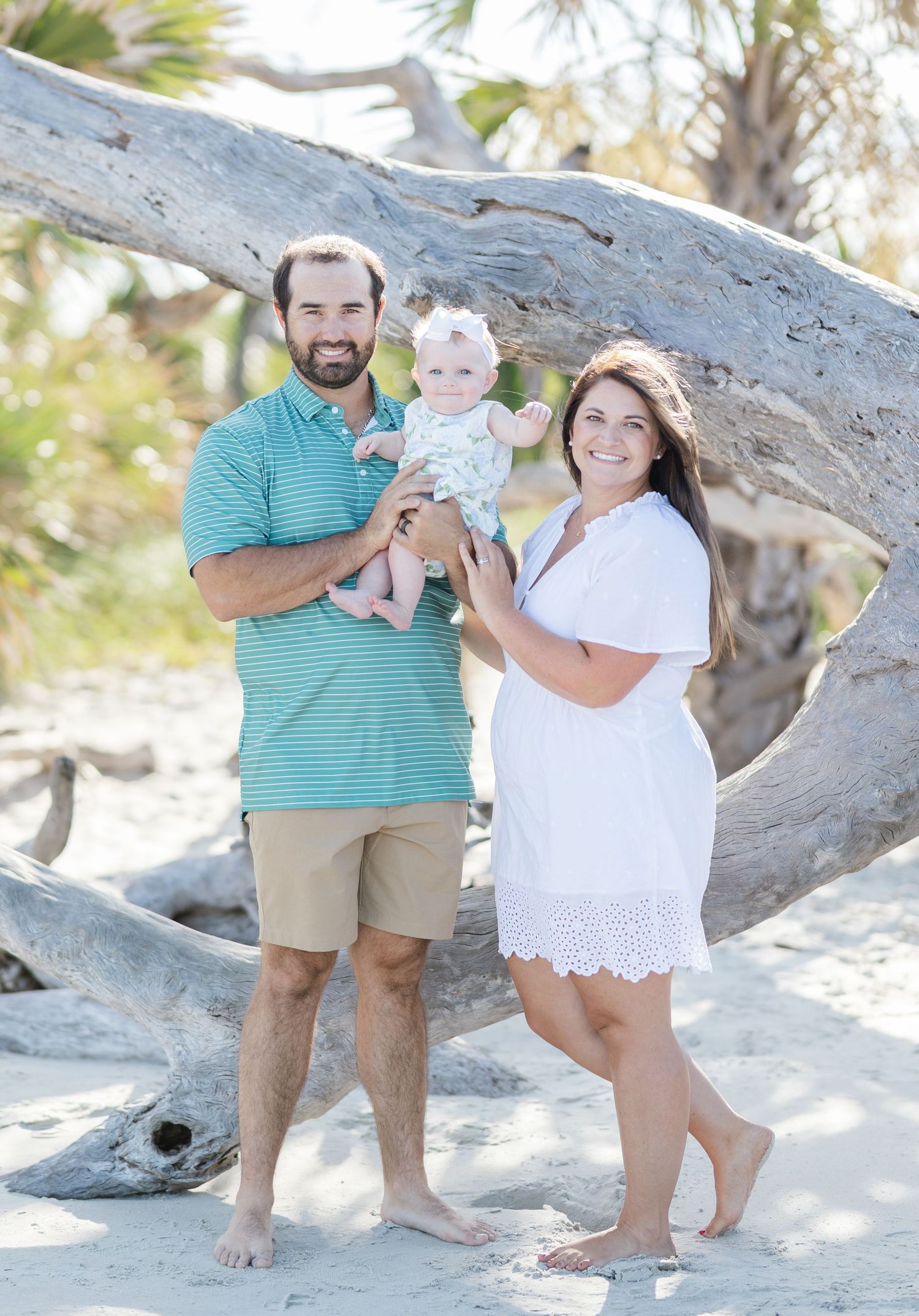 Family enjoying a beach day together by driftwood log on sandy shore with palm trees in background.