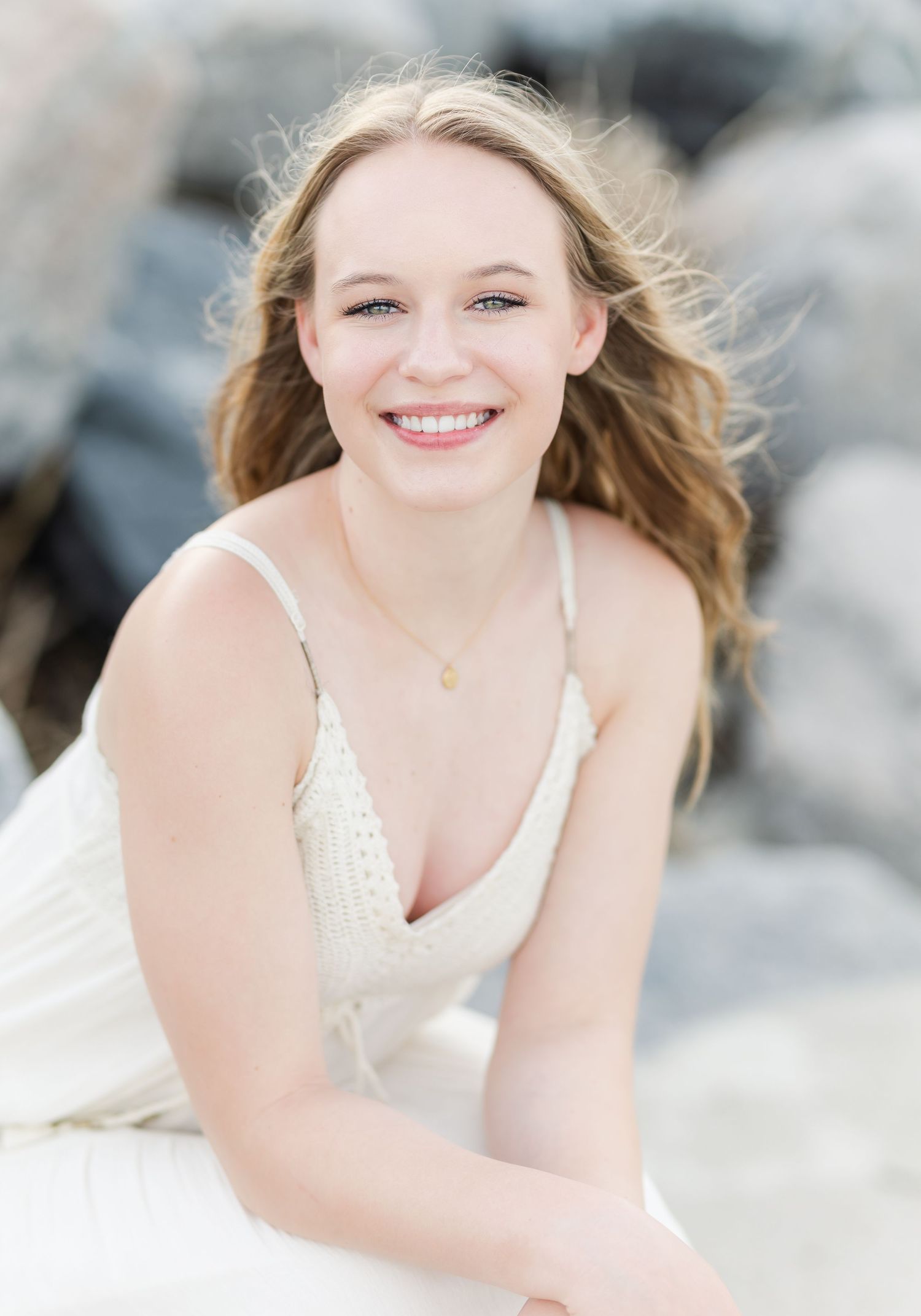 Soft ethereal beach portrait with white dress against rocky coastal background.