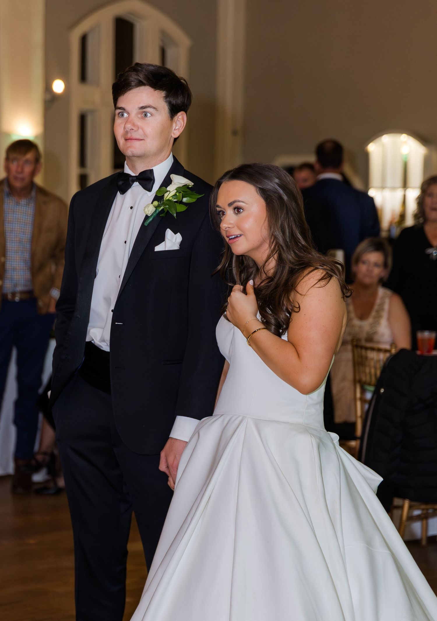Bride in white ball gown and groom in black tuxedo share a moment on the dance floor at elegant wedding reception.