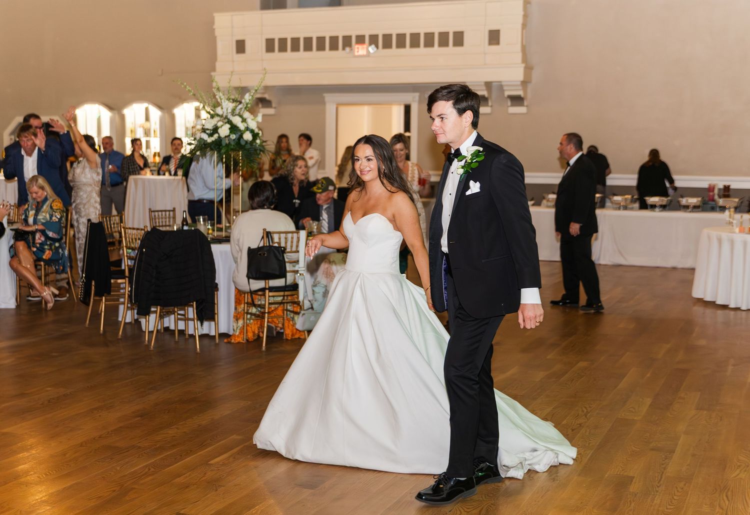 Bride in white ball gown and groom in black tuxedo share first dance at elegant wedding reception.