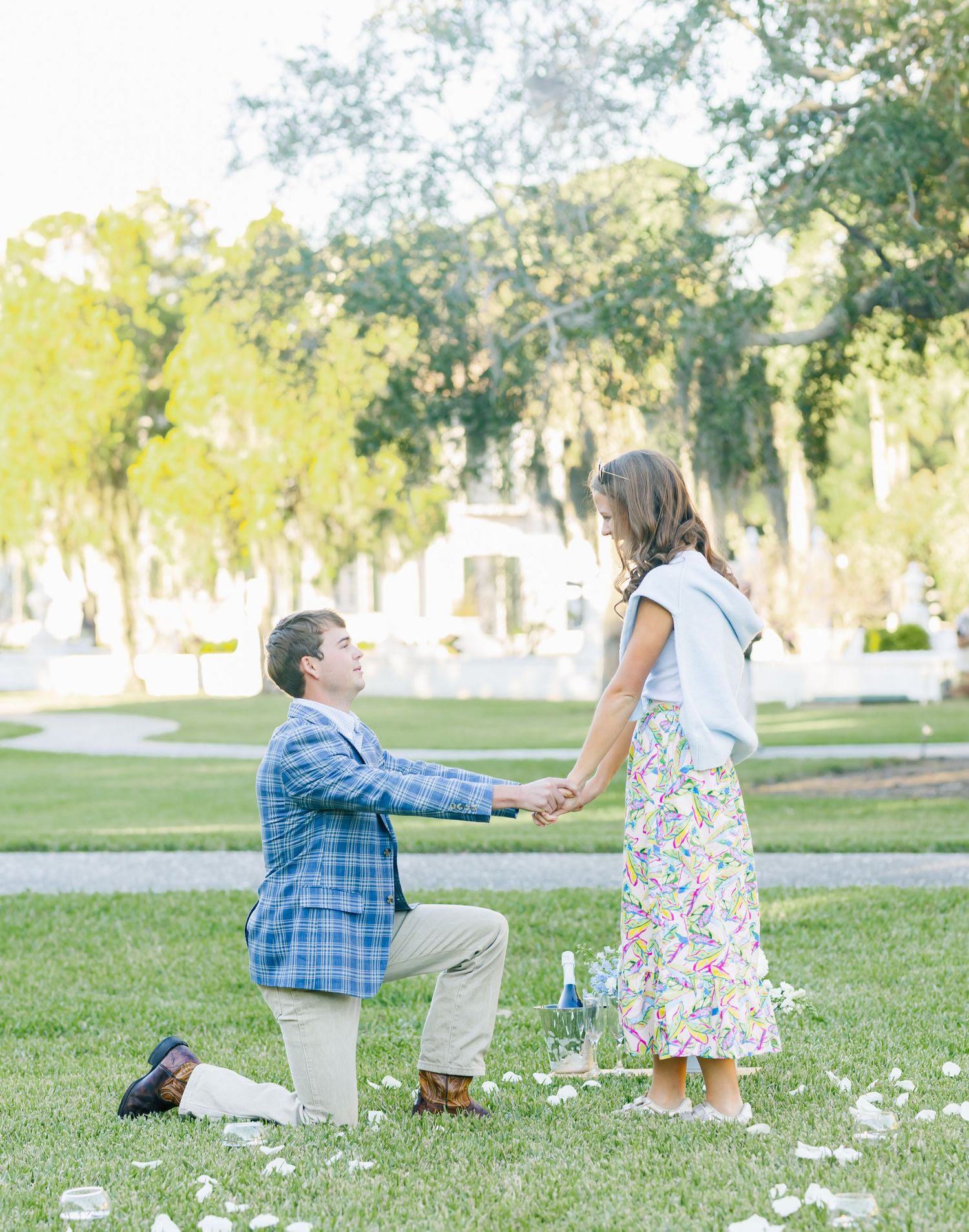A couple shares a romantic moment in a park setting with wildflowers and trees in the background.