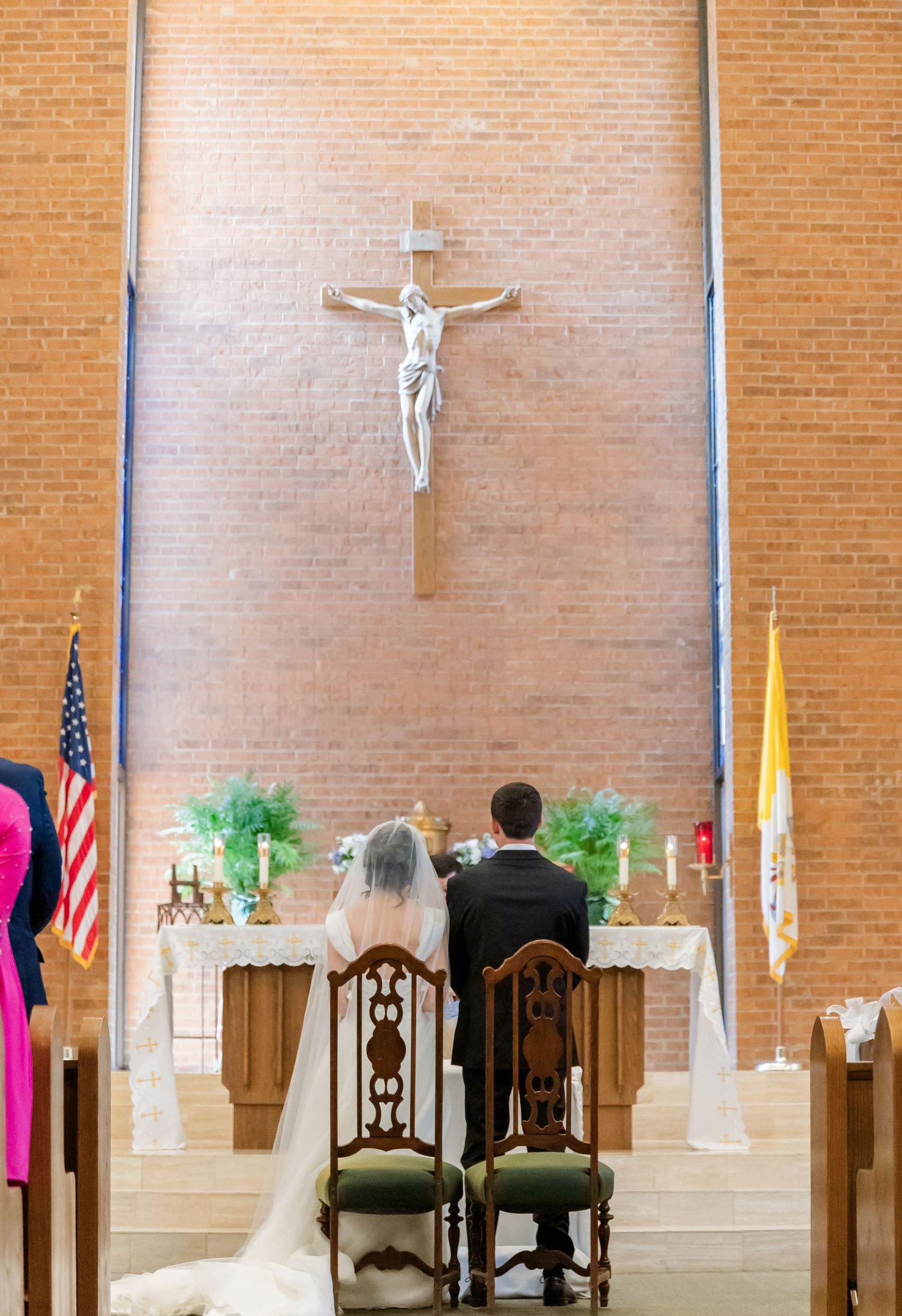 A couple kneels at the altar during their Catholic wedding ceremony beneath a large crucifix.