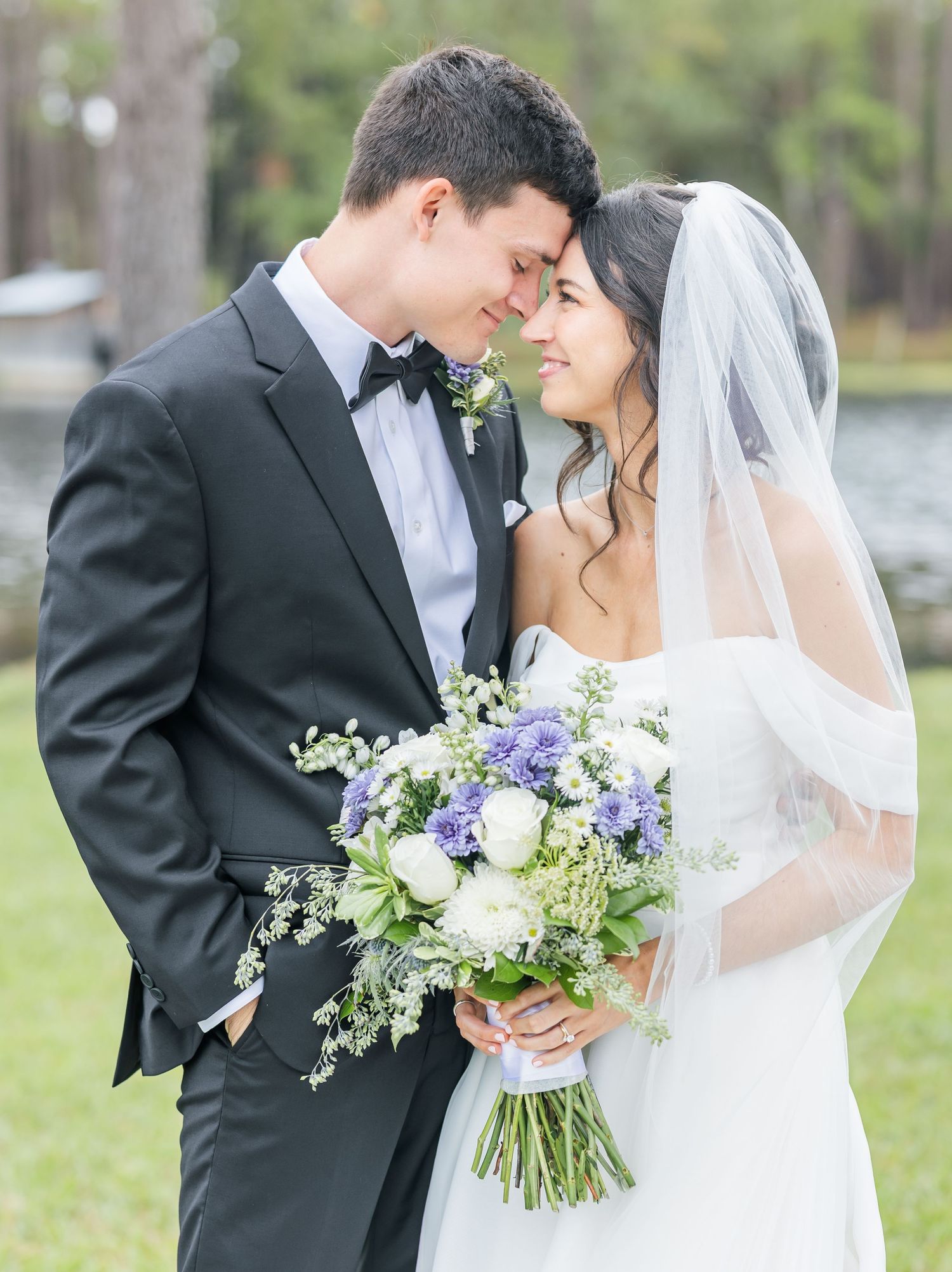 Romantic wedding couple shares intimate moments outdoors with purple and white floral bouquet.