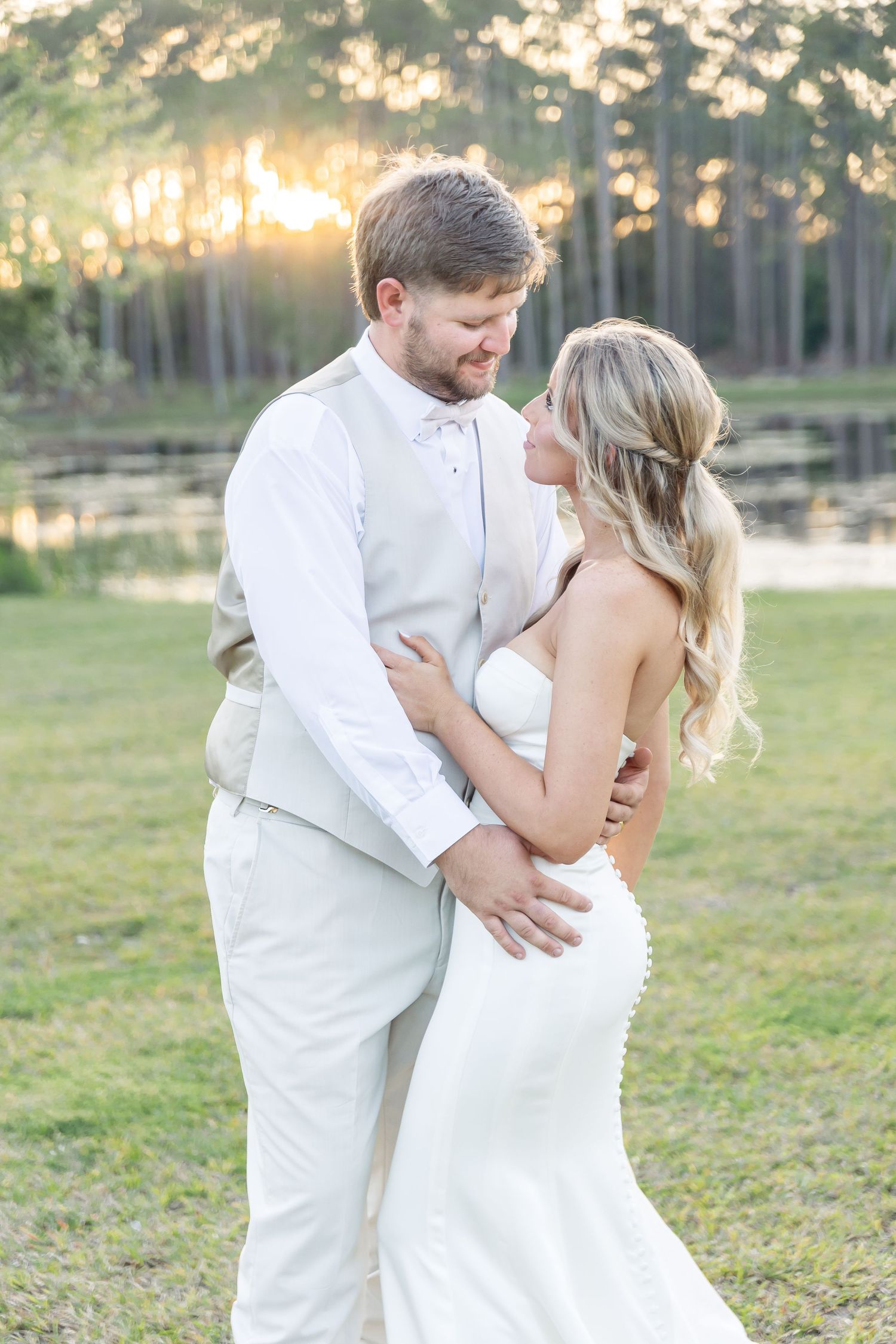 Romantic lakeside wedding portrait with glowing sunset and pine trees in the background.