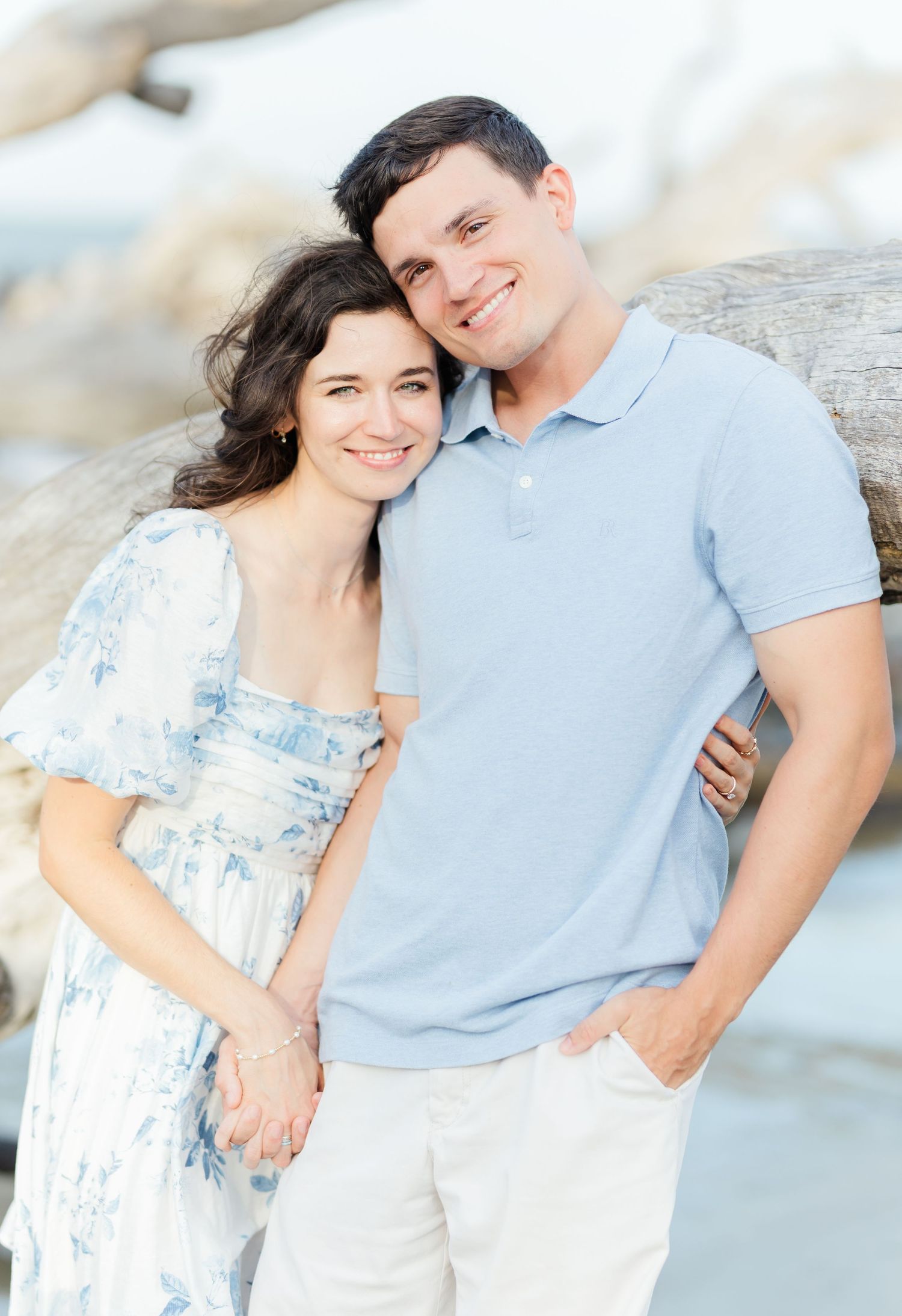 A tender moment between a couple in coordinated blue outfits against a bright coastal background.