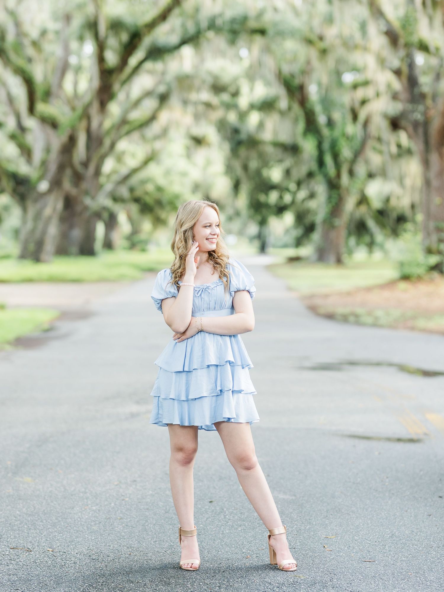 A dreamy outdoor photoshoot in a light blue ruffled dress against a tree-lined path.