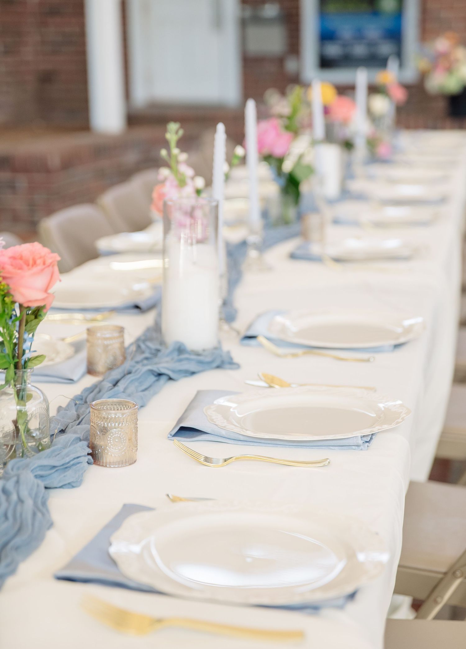 Elegant dining table setting with light blue napkins, white plates and single coral roses in small vases create a romantic atmosphere.