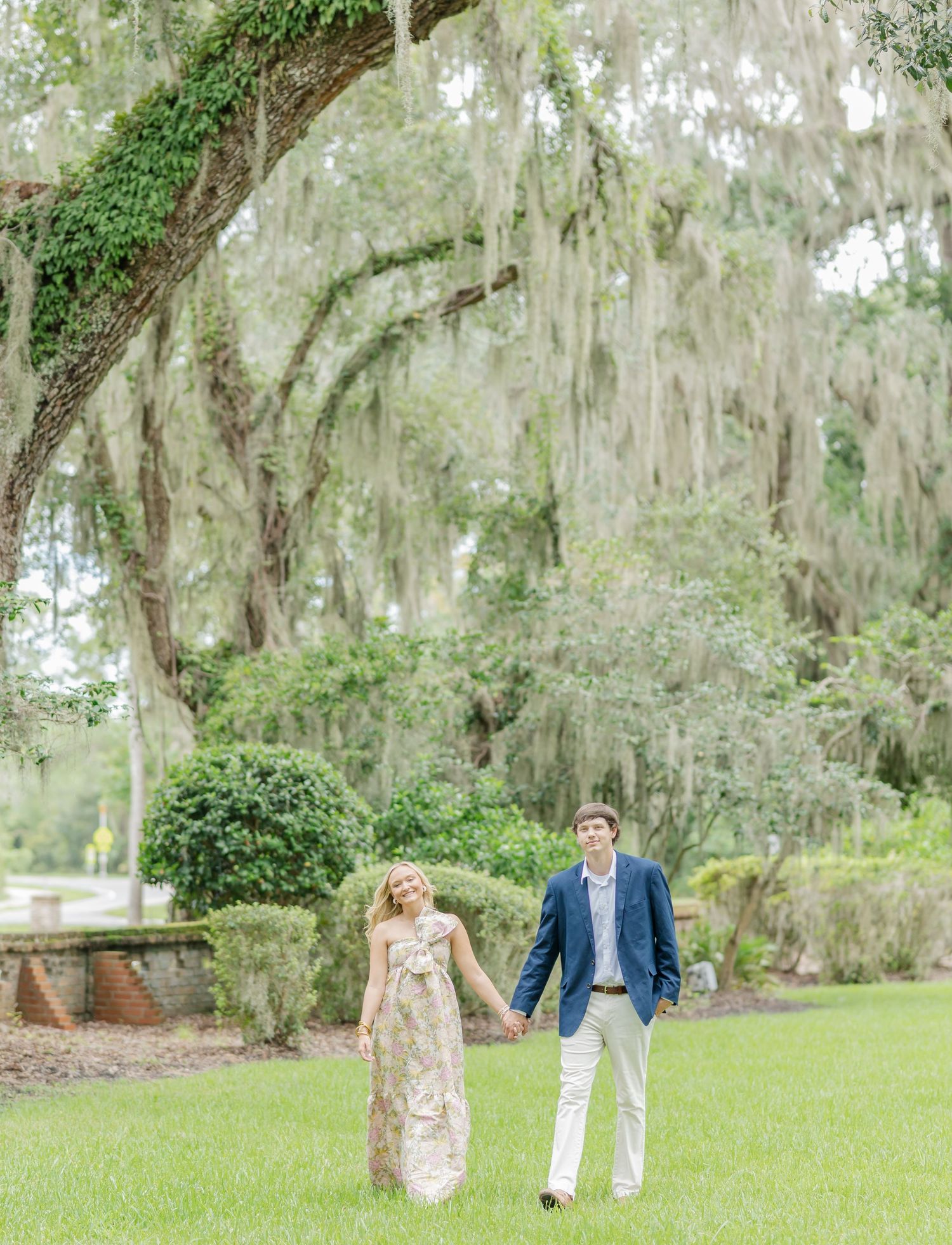 A couple walks through a scenic garden path with Spanish moss draped trees creating a romantic atmosphere.