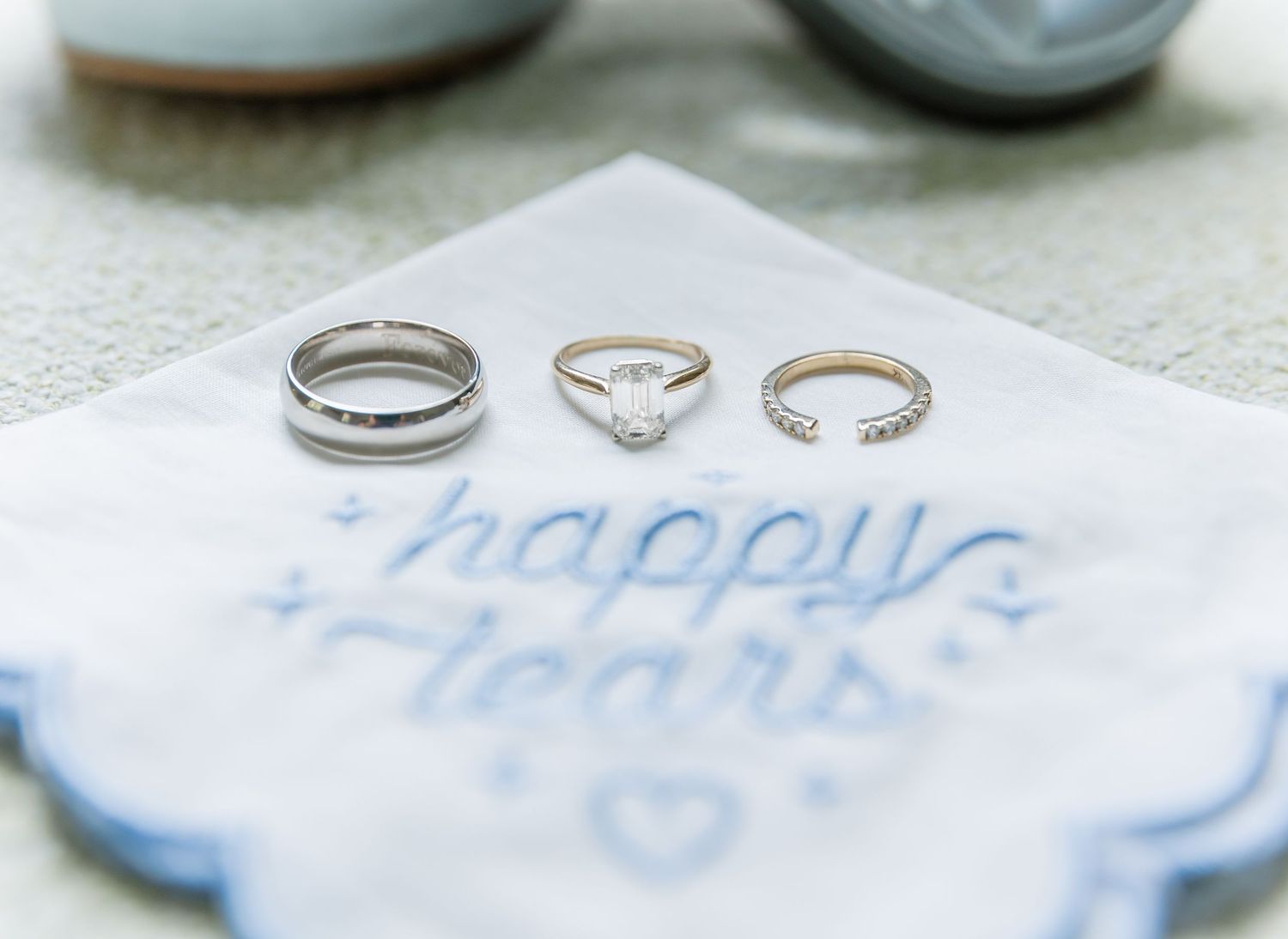 Three wedding rings arranged on white embroidered handkerchief with blue text.