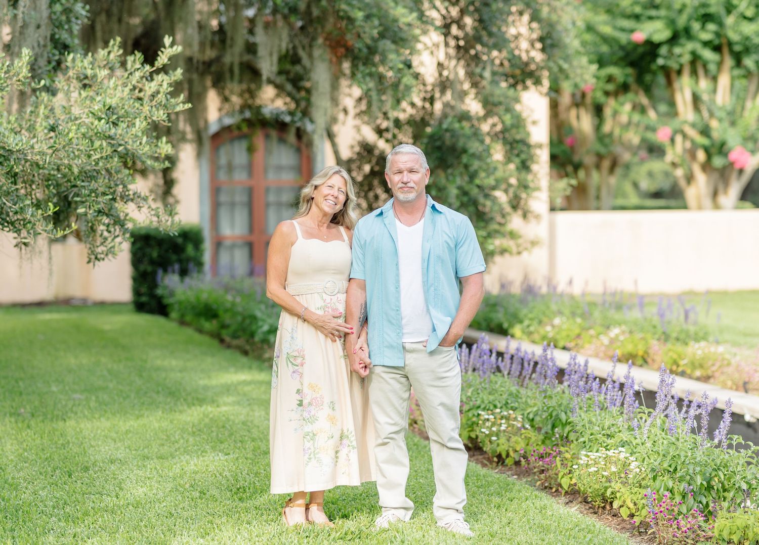 A couple walks together through a lush garden pathway with beautiful purple flowering borders.