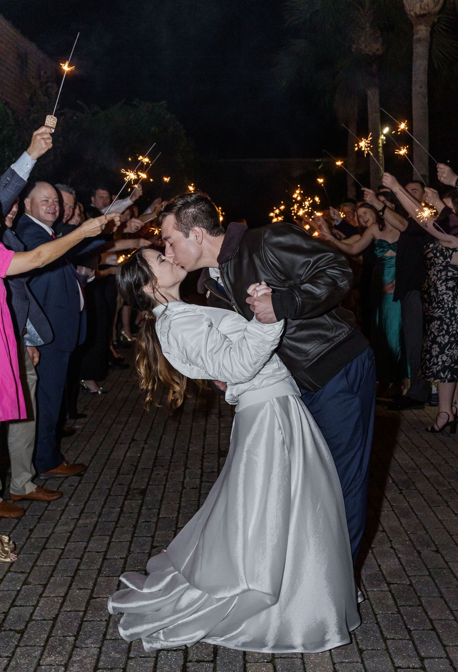Wedding couple dances outdoors at night surrounded by guests holding sparklers during their romantic celebration.