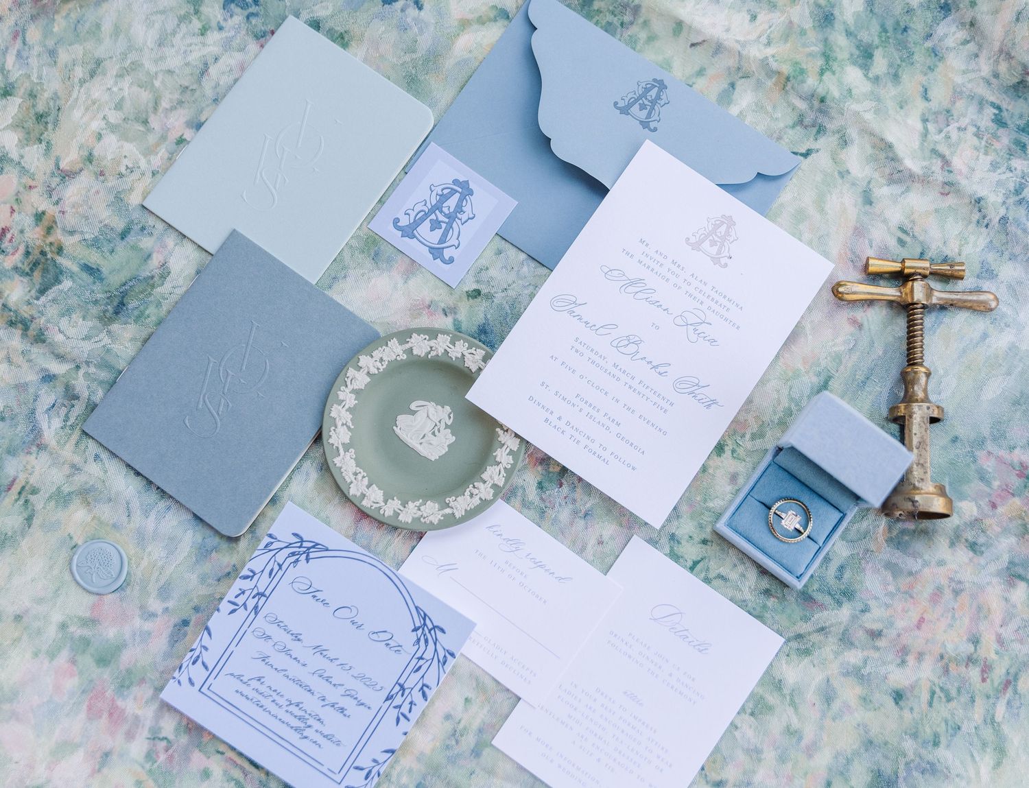 Wedding invitation flat lay with blue envelopes, crystal crown and vintage brass bell on floral background.