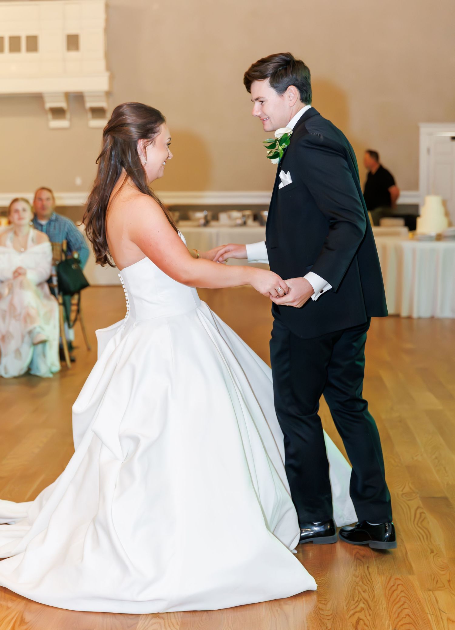 Bride and groom share their first dance at wedding reception, bride in white ballgown, groom in black tuxedo.