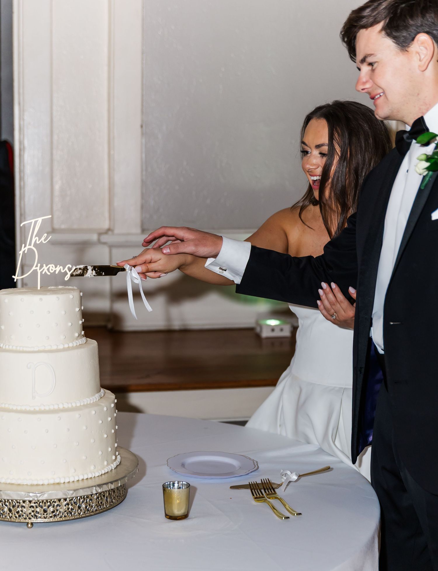 Bride and groom cutting their white three-tier wedding cake together at their elegant reception.
