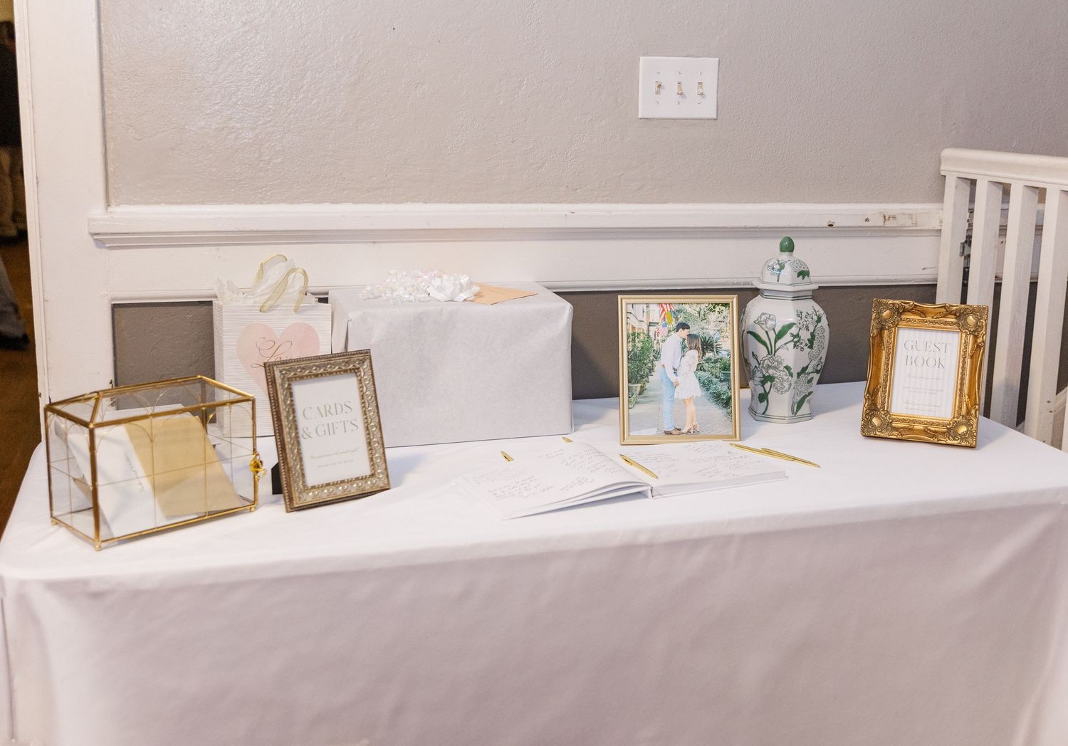 Elegant wedding gift table with gold frames, card box, floral arrangement, and white tablecloth at a reception.
