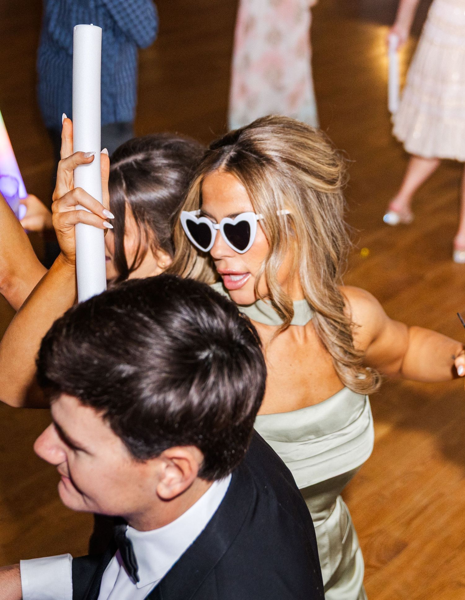 Wedding guest in heart-shaped white sunglasses dancing at lively wedding reception.