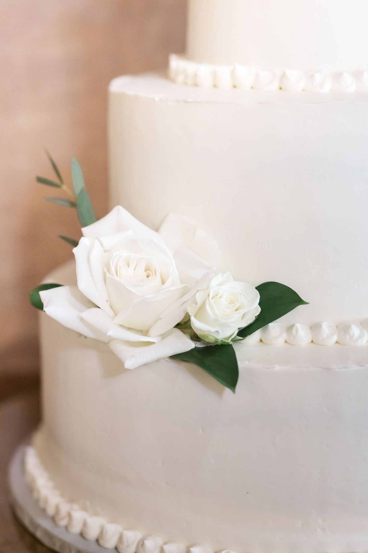 Elegant white wedding cake decorated with fresh white roses and delicate pearl details.