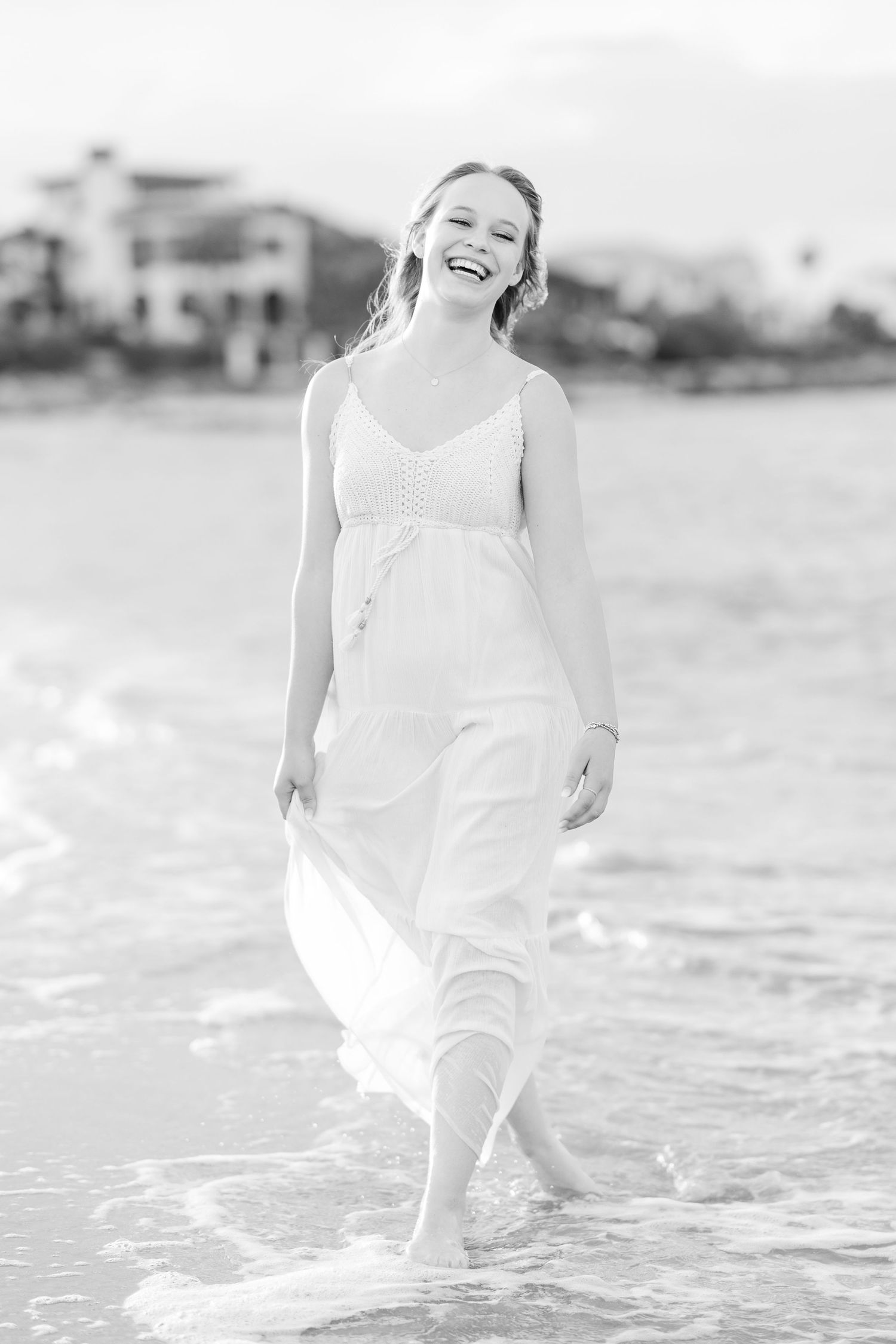 A series of black and white photos showing someone playing in shallow ocean waves wearing white clothing.
