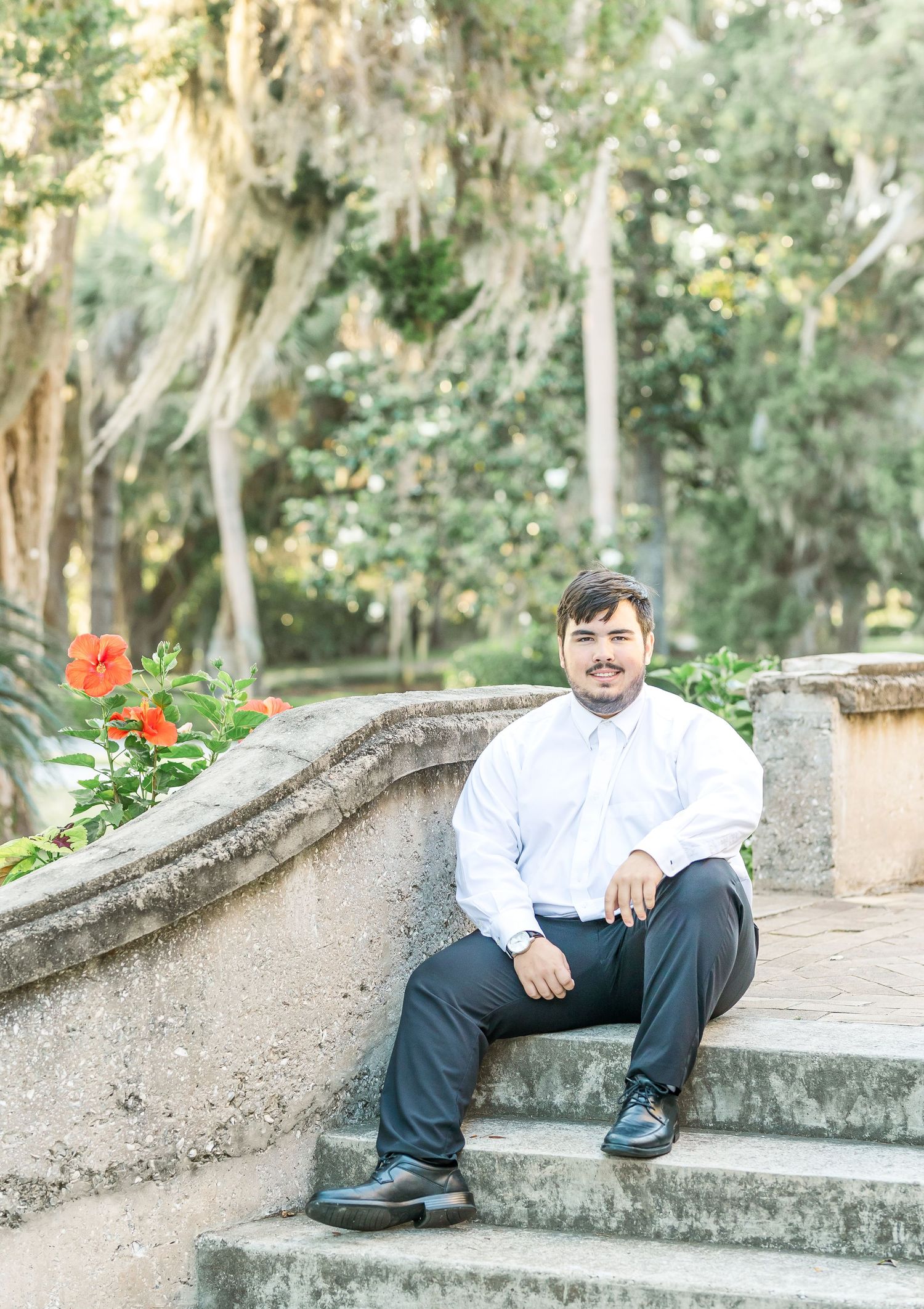 Person in white shirt sitting on concrete steps in front of lush garden background and trees.