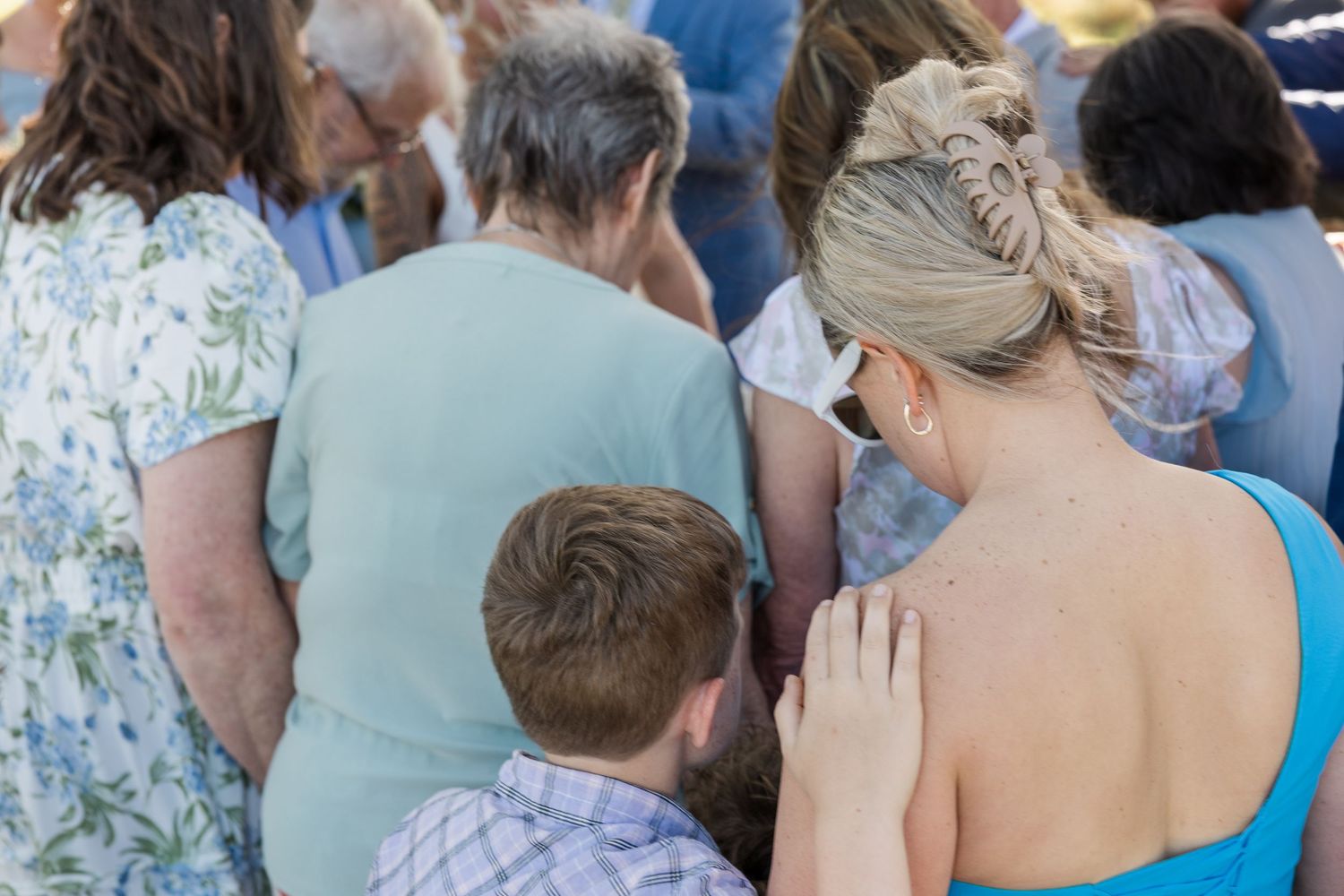 Wedding guests bowing heads in prayer during an outdoor ceremony on a sunny day.