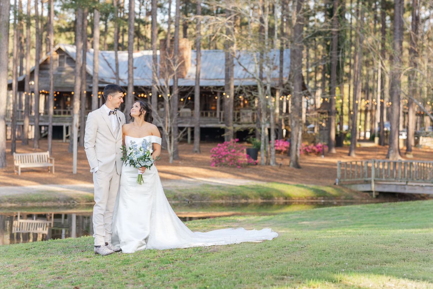 Bride and groom portrait in front of rustic log cabin venue with pond reflection at outdoor wedding.