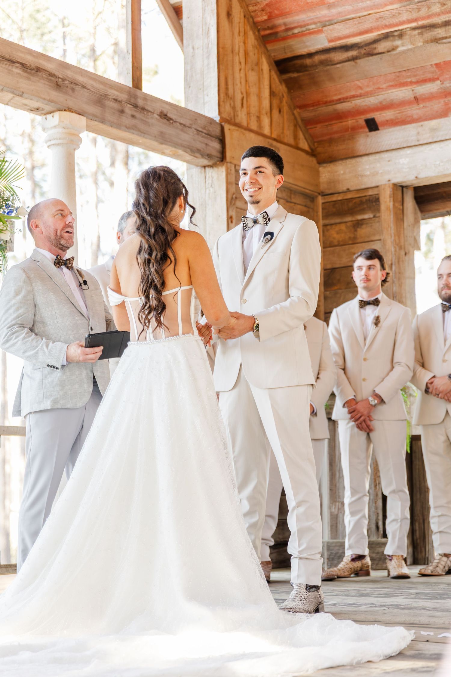 Bride and groom holding hands at altar during rustic outdoor wedding ceremony with groomsmen.