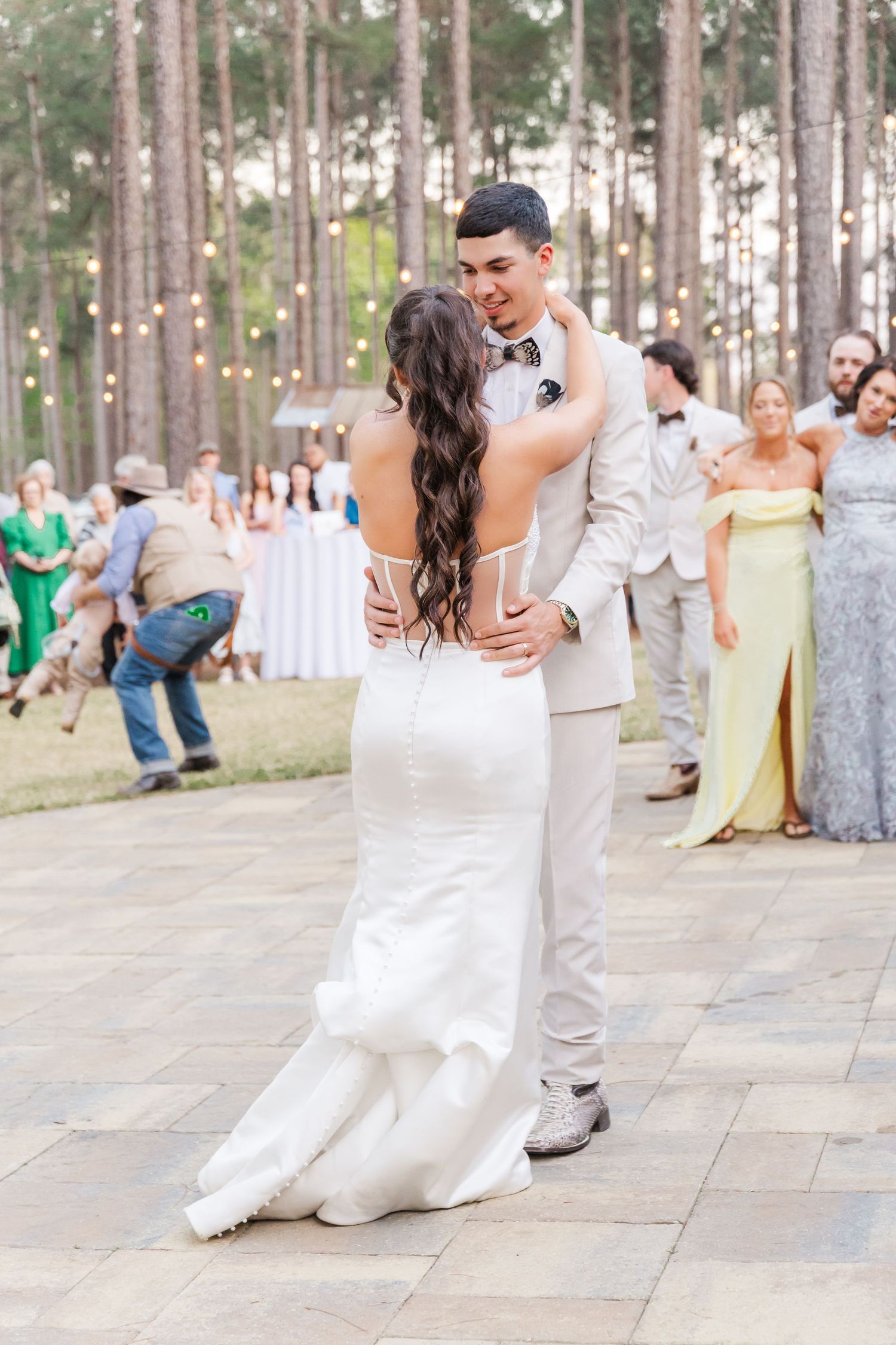 Bride and groom share their first dance on an outdoor stone floor surrounded by wedding guests.