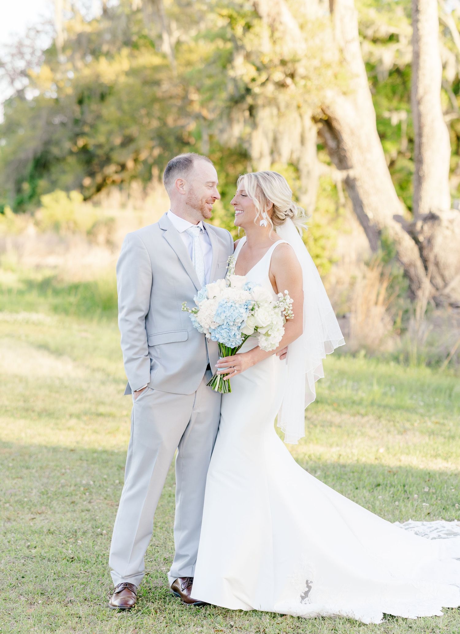Bride and groom share romantic moment outdoors, bride holding blue hydrangea and white rose bouquet.