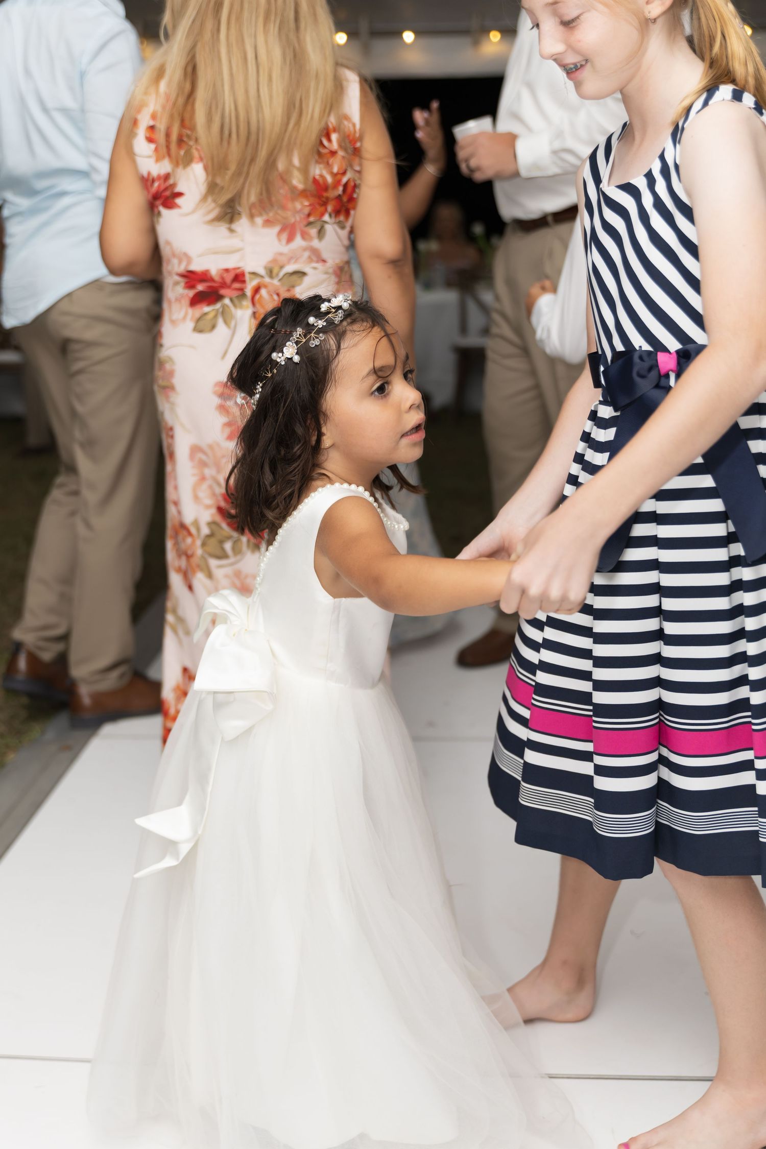 Children in white and striped dresses dance together at a festive celebration.