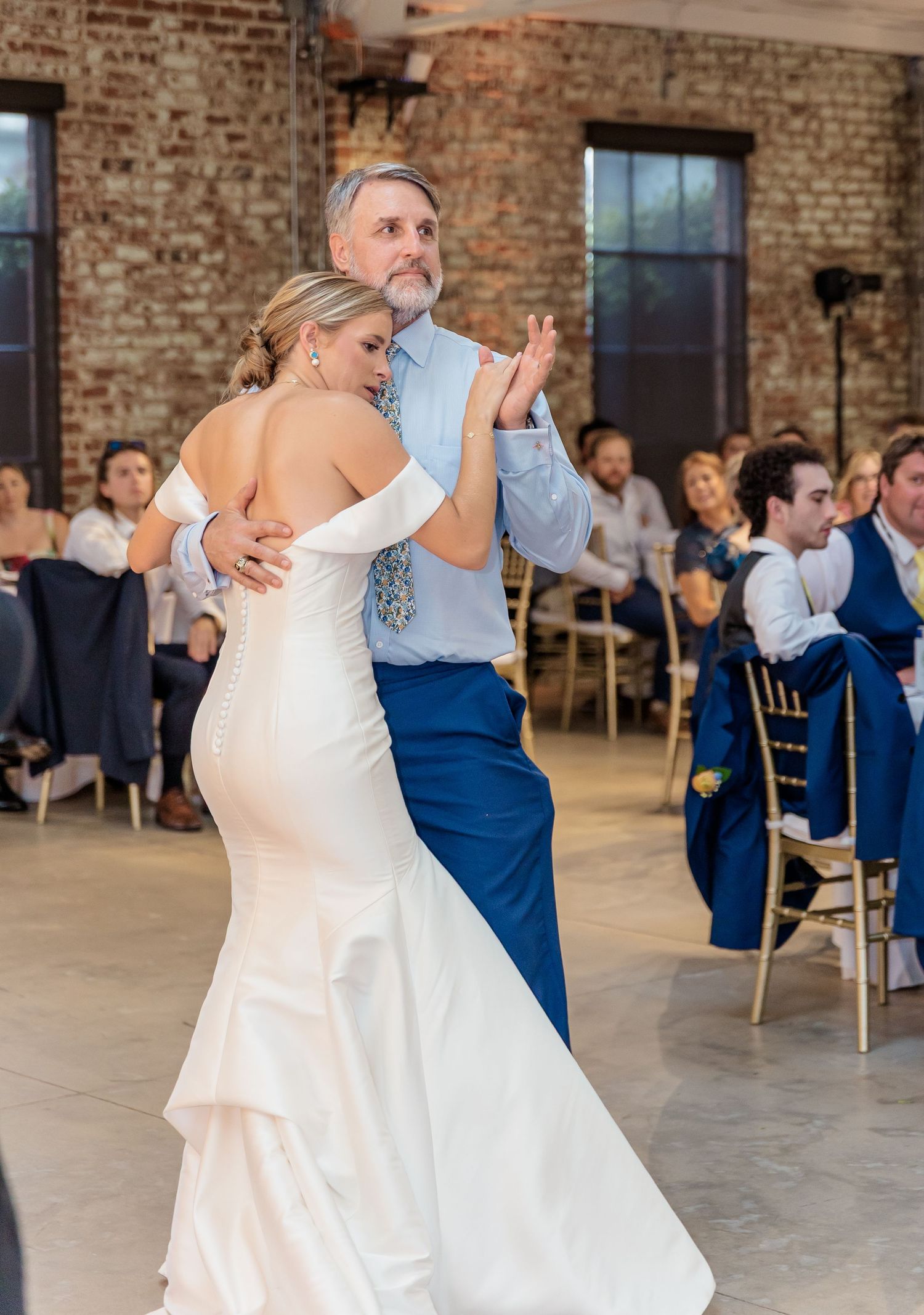 Couples dance together during a wedding reception in an elegant brick-walled venue with natural lighting.