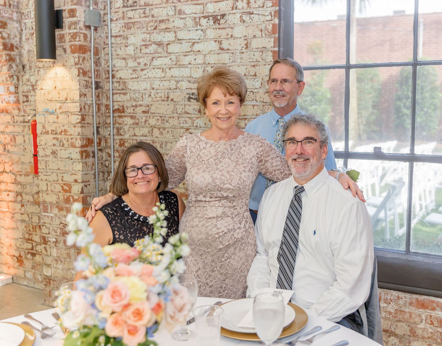 A group gathers at a rustic brick venue for a wedding reception celebration with floral centerpieces.