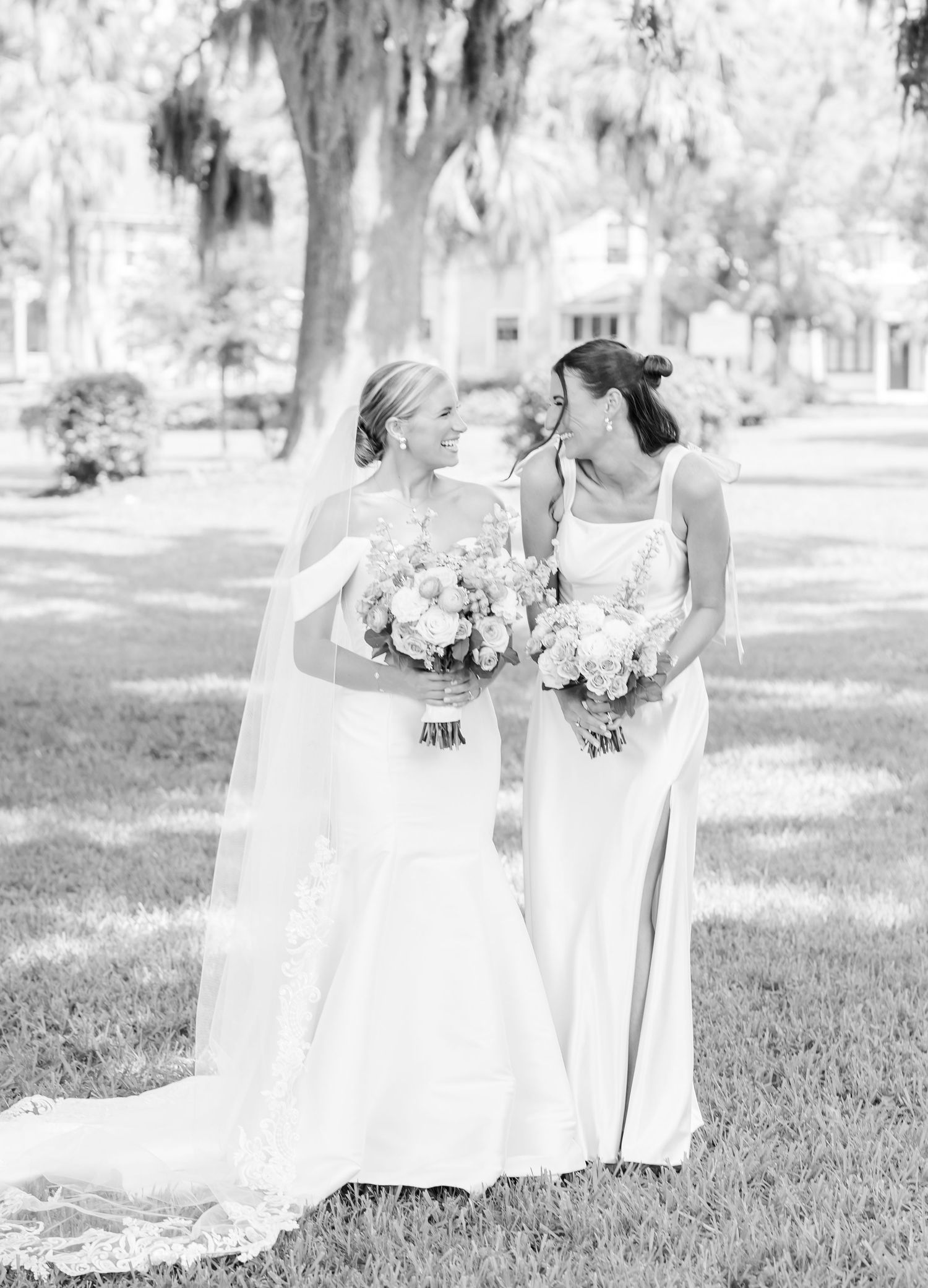 Black and white photo of bridal party holding bouquets while standing on grass under trees.