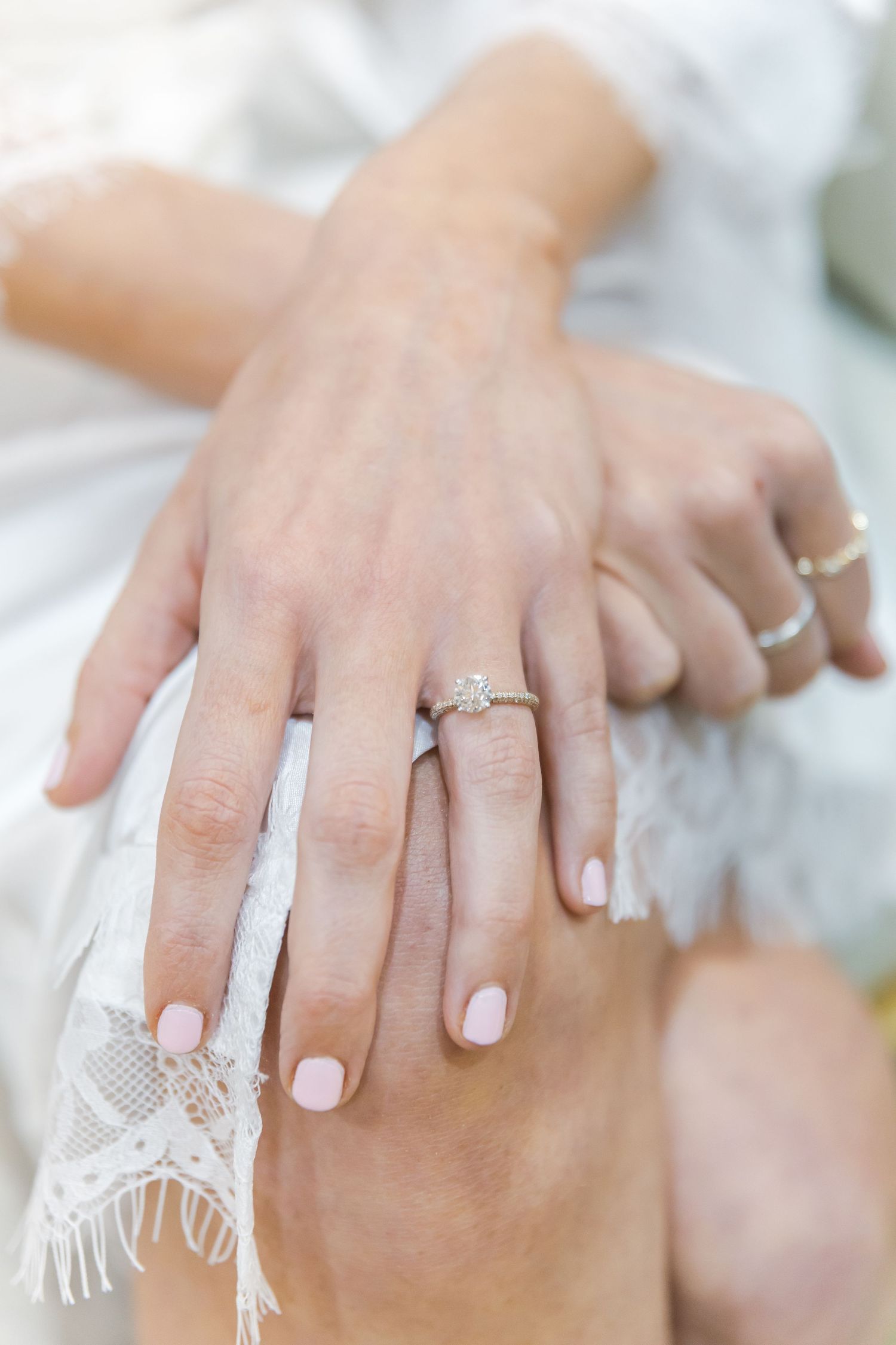 Several hands displaying engagement rings with manicured nails against a light background.