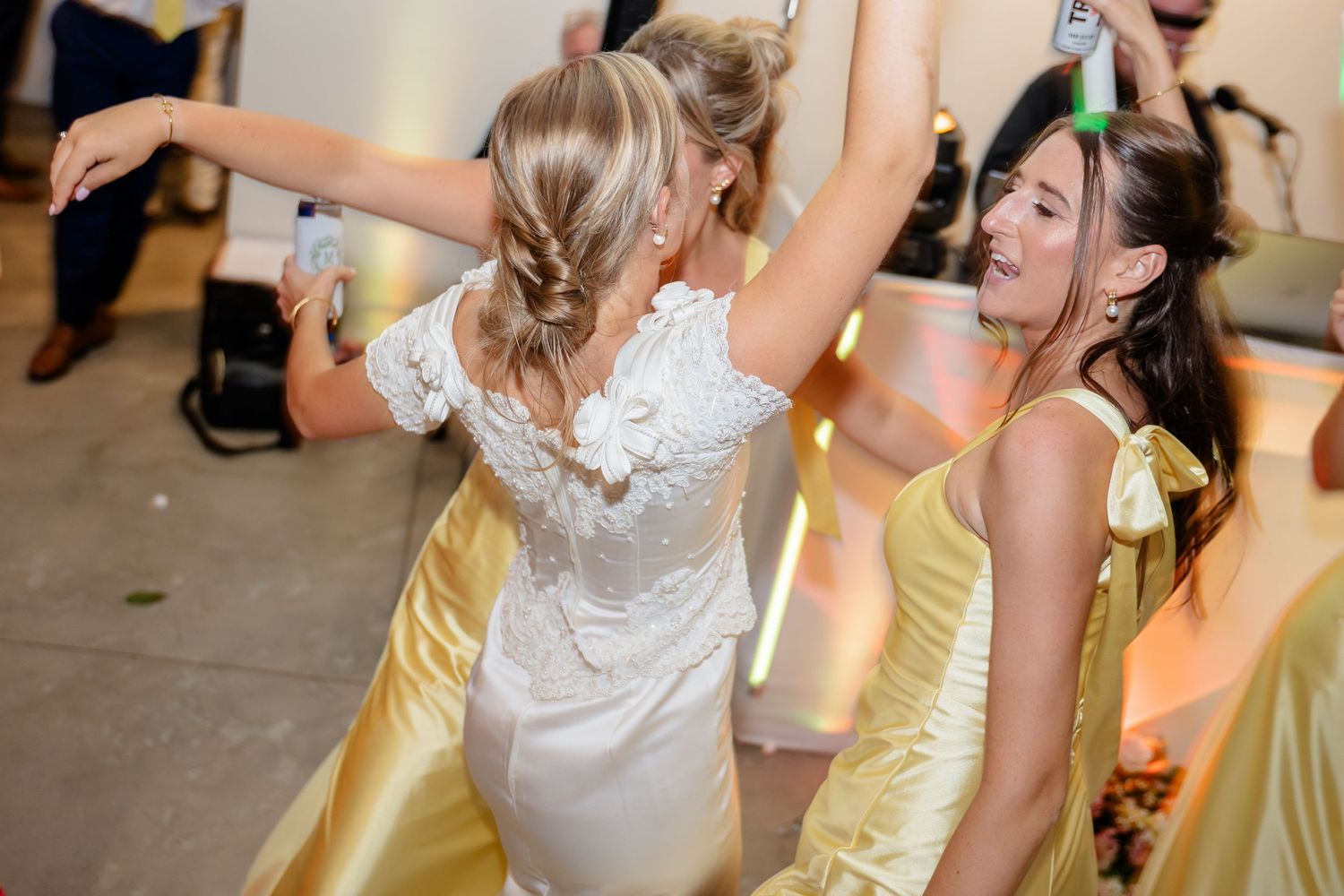 Partygoers in yellow and white dresses dance with illuminated foam batons.