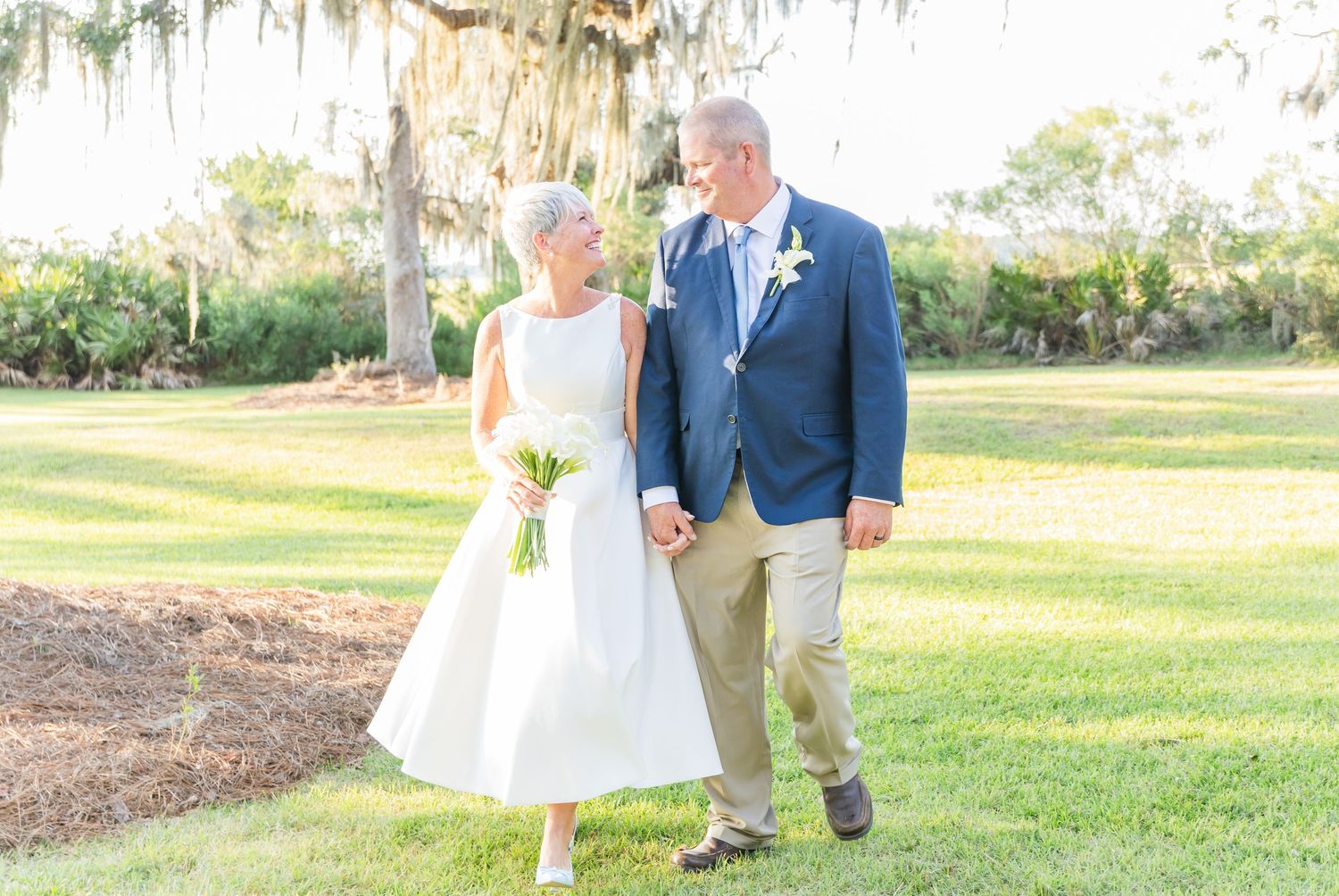 A romantic outdoor wedding ceremony takes place under Spanish moss draped trees in a serene garden setting.