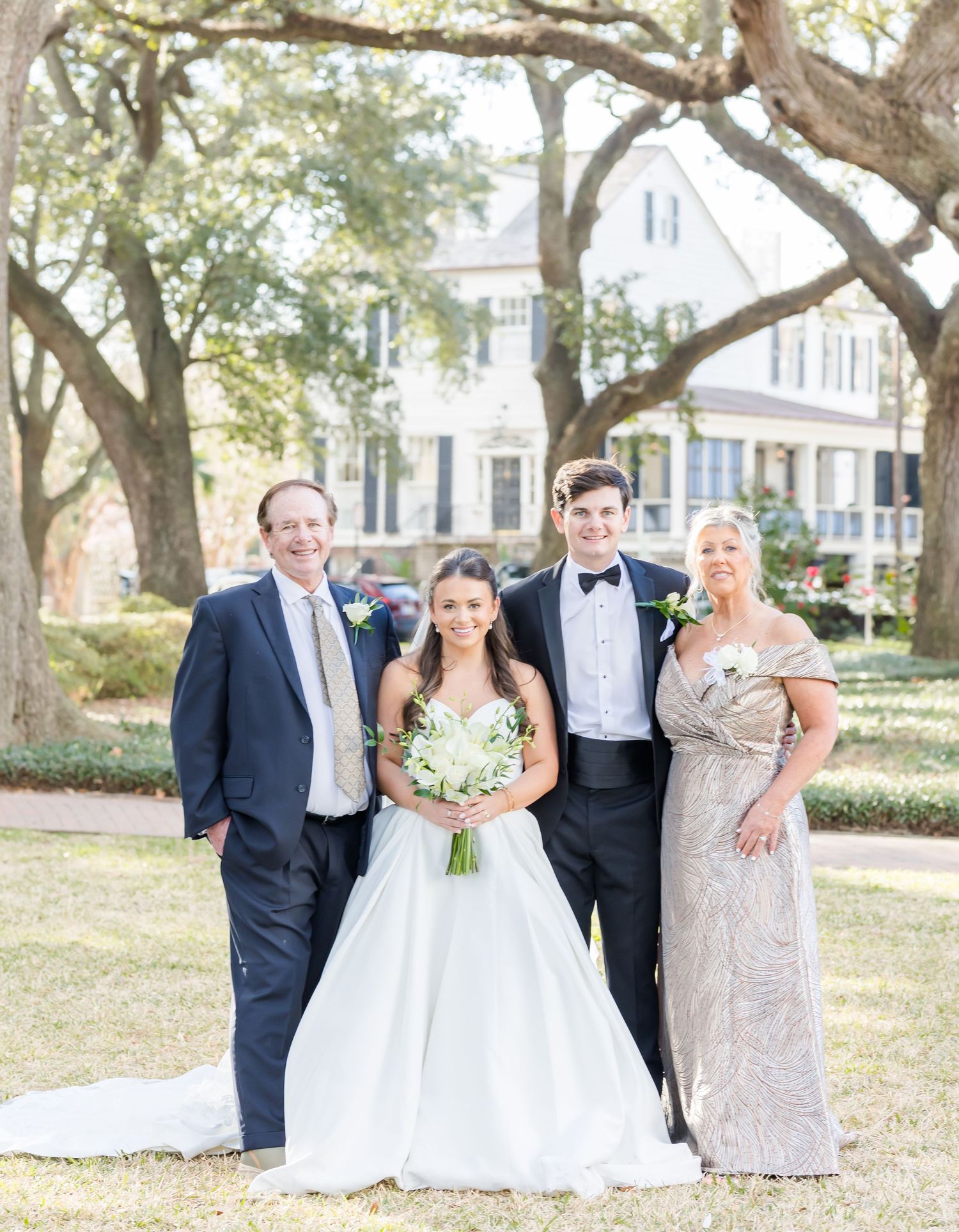 Wedding party poses for formal portraits under large oak trees on a sunny day.