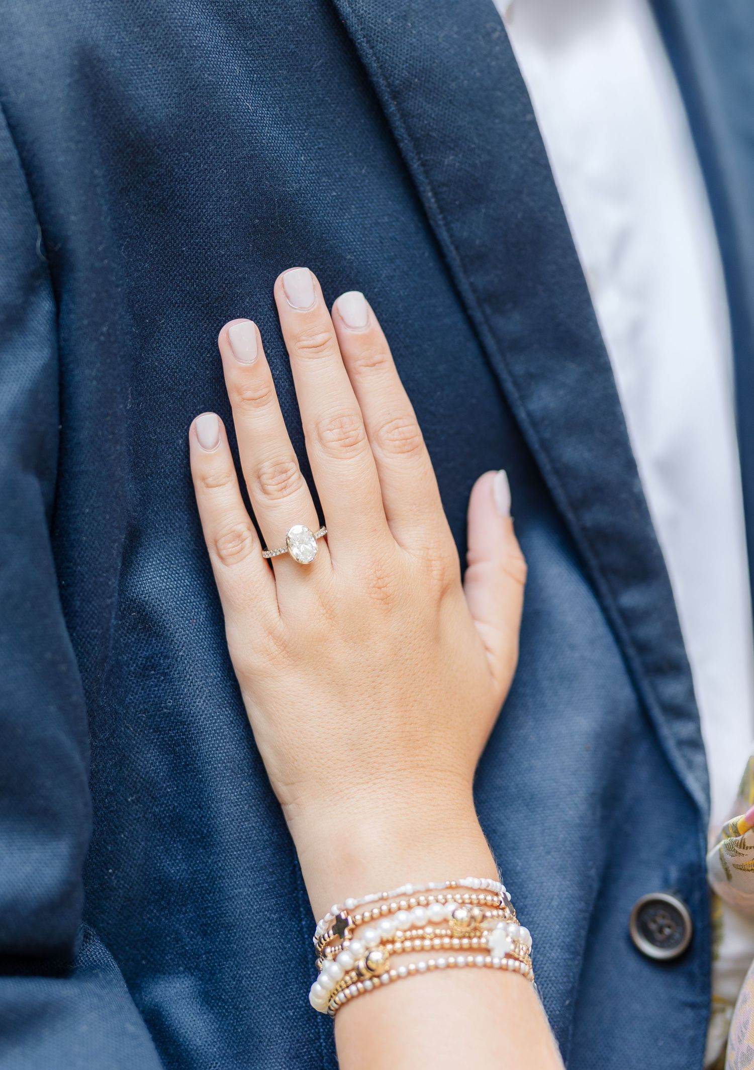 Close-up sequence of hands showing engagement ring and pearl bracelets against a navy blue suit jacket.