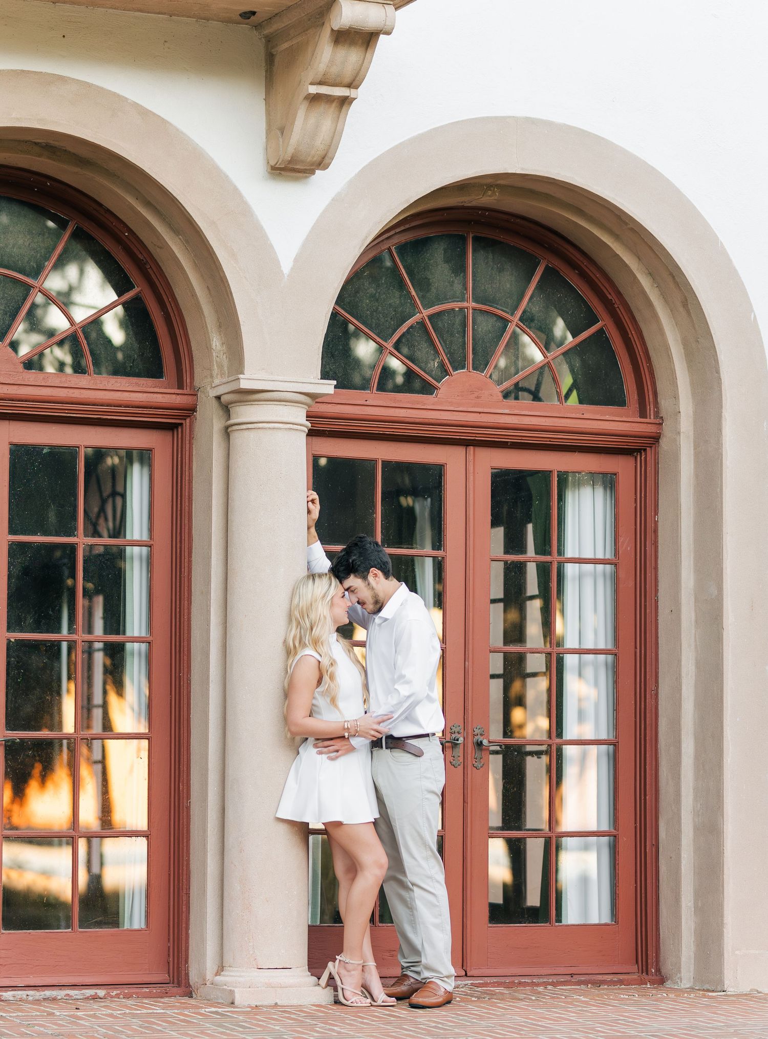 A romantic couple shares tender moments under arched columns at sunset.