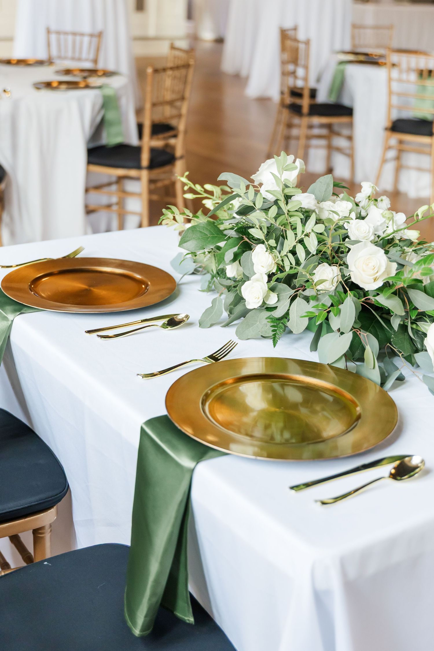 Wedding table settings featuring white linens, gold charger plates, and fresh eucalyptus centerpieces.