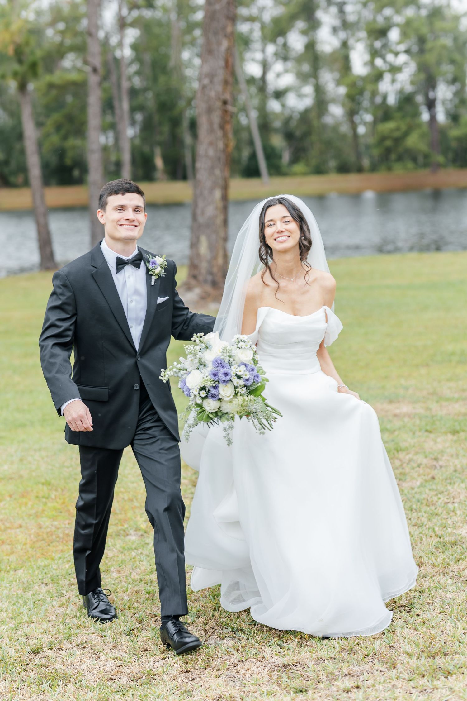 Wedding couple poses casually on lawn with lake and trees in background.