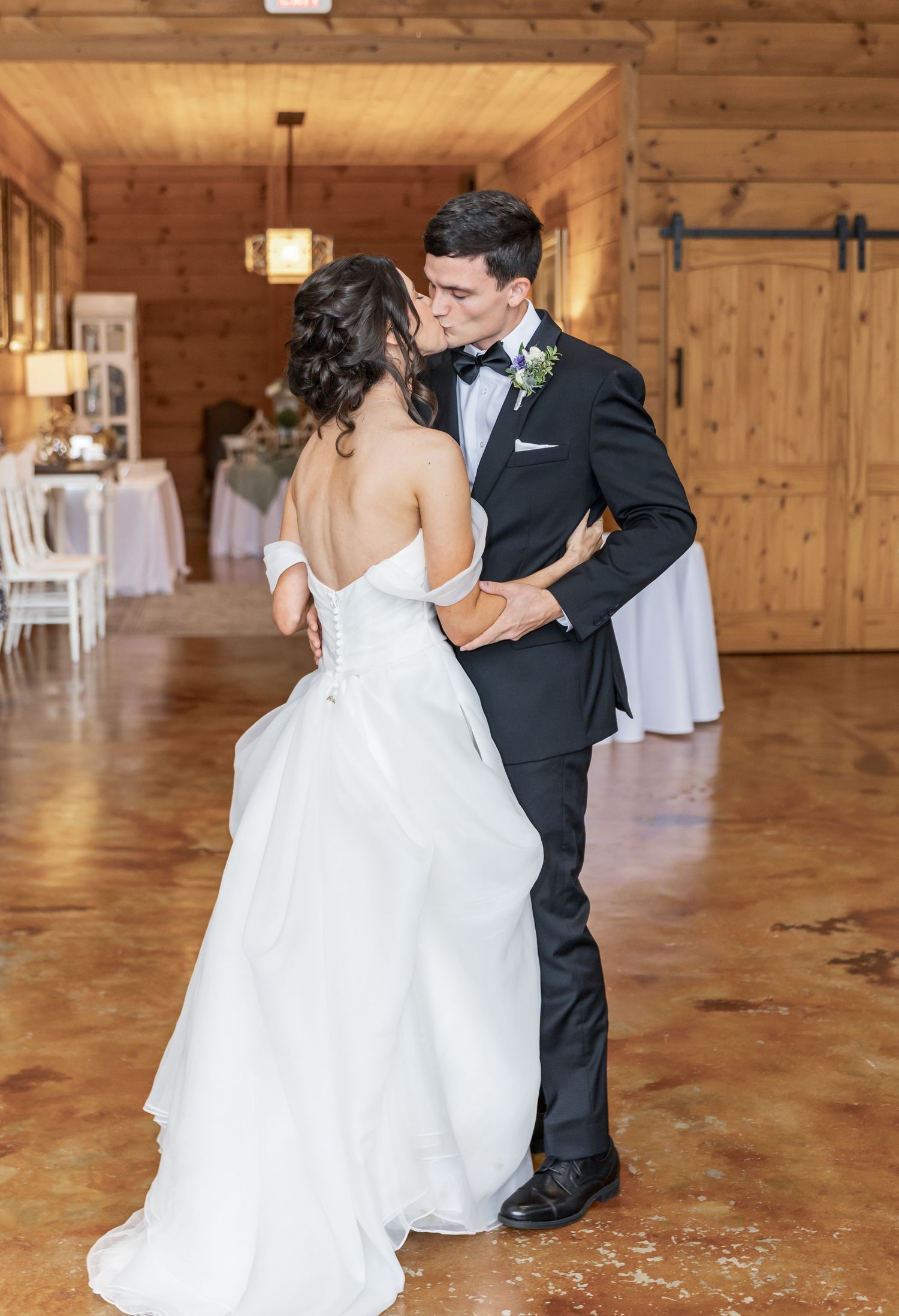 Wedding couple shares romantic dance on wooden reception venue floor.