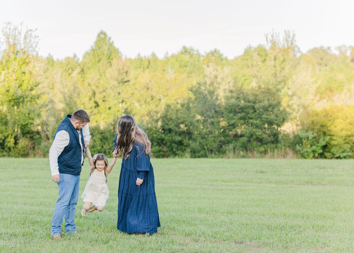 A family stands together in a sunlit green field with trees in the background during golden hour.