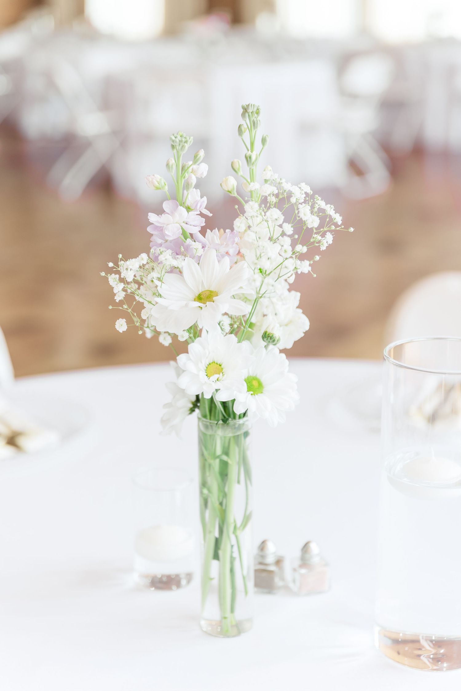 Simple white floral centerpiece with baby's breath in a glass vase on a white tablecloth.
