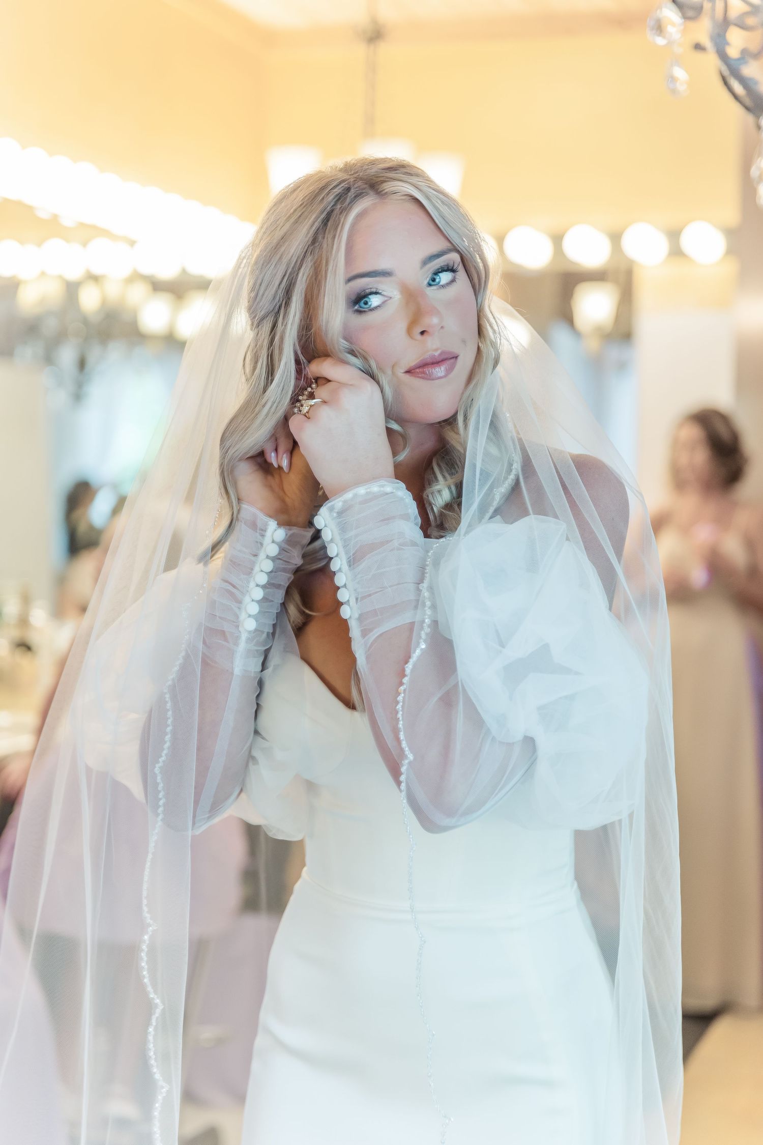 A dreamy bridal portrait featuring a classic white wedding dress with sheer sleeves and long veil.